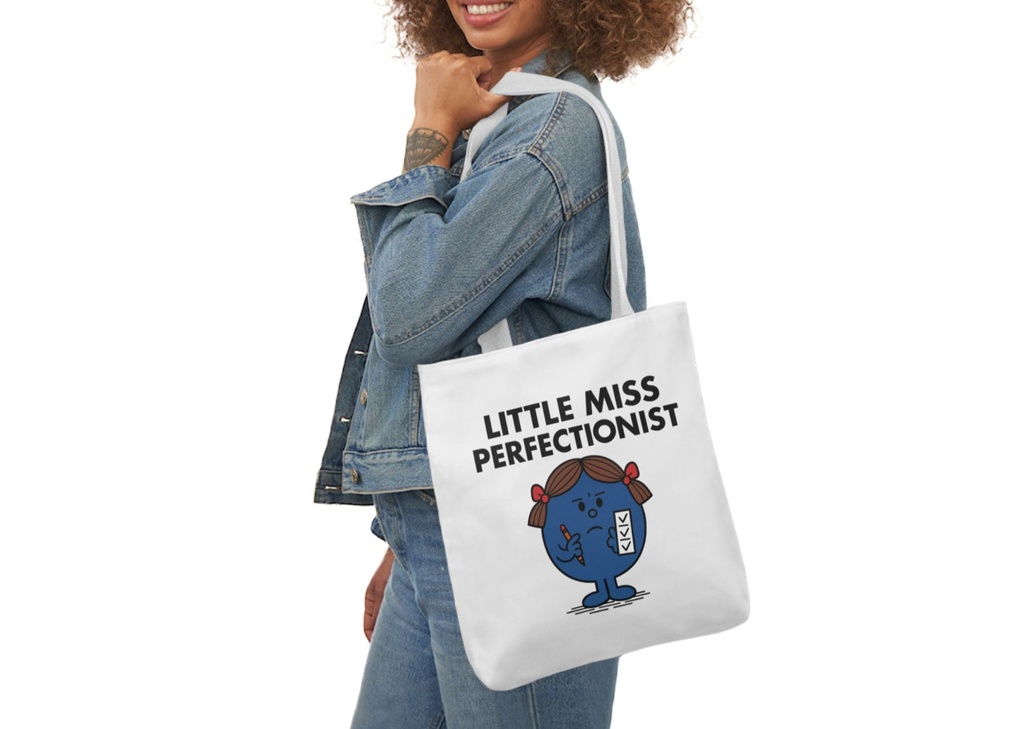 Woman in denim modeling the Little Miss Perfectionist tote over her shoulder. She smiled, but internally she's critiquing the kerning. Part of the Vivid Divergence Little Miss Meme Collection!