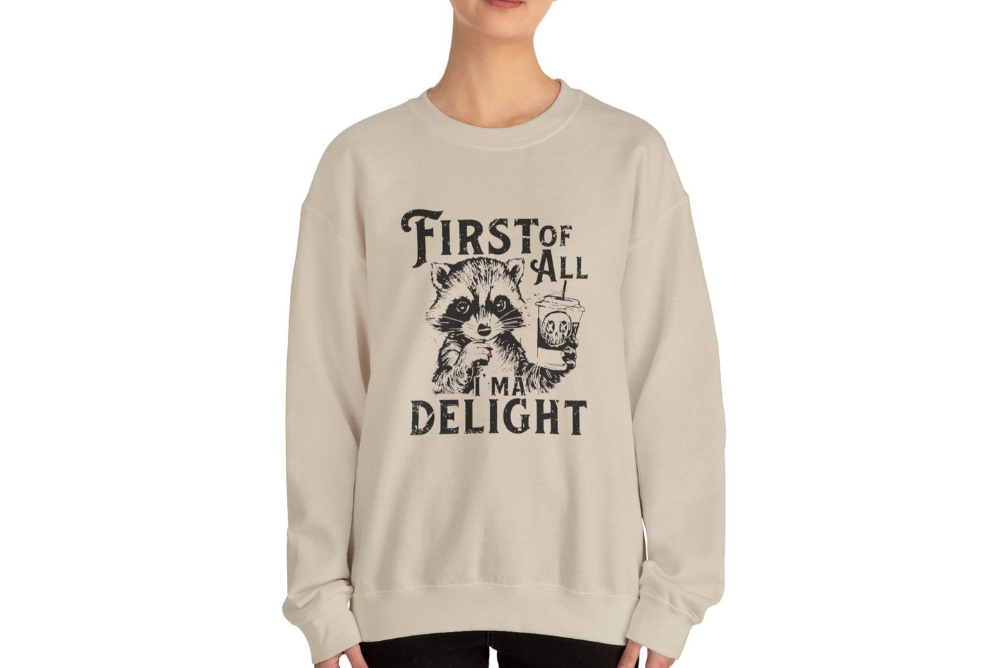 Model wearing a beige sweater jumper with the text "First of All, I’m a Delight" and a cartoon raccoon illustration. Part of the Vivid Divergence Sensory Friendly Unisex Sweater Jumper Range.