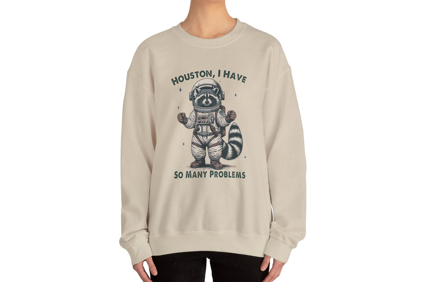 Model wearing a beige sweater jumper with the text "Houston, I Have So Many Problems" and a cartoon raccoon illustration holding a striped object. Part of the Vivid Divergence Sensory Friendly Unisex Sweater Jumper Range.