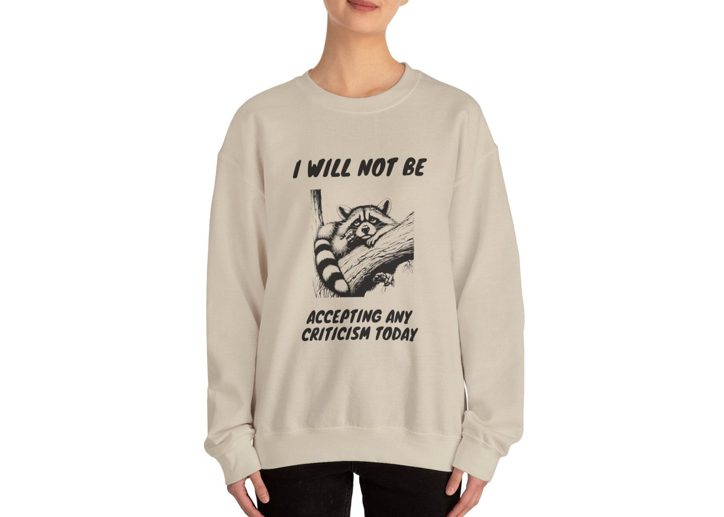 Model wearing a beige sweater jumper with the text "I Will Not Be Accepting Any Criticism Today" and a cartoon illustration of a hand with a raised finger. Part of the Vivid Divergence Sensory Friendly Unisex Sweater Jumper Range.