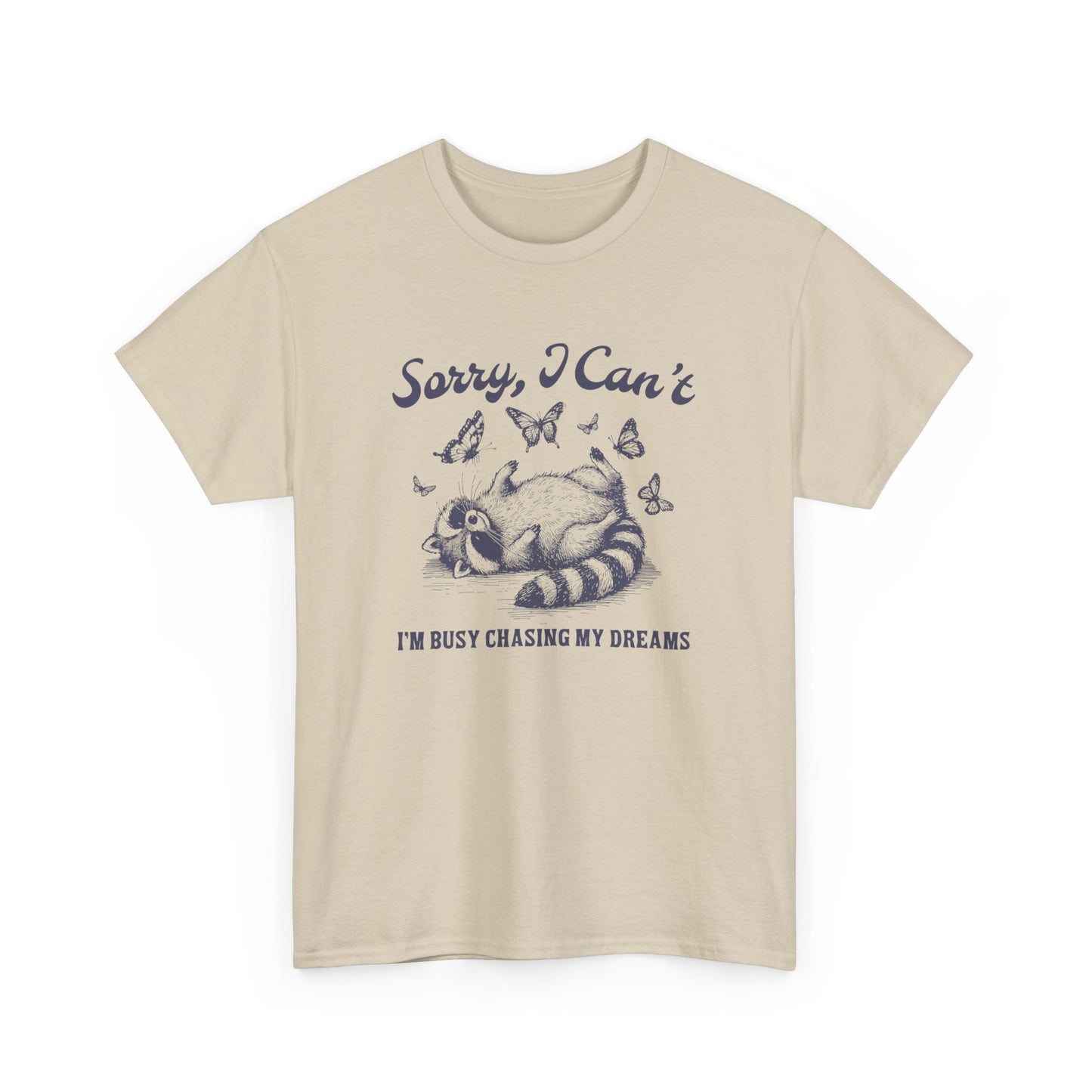 Front view of a beige T-shirt with "Sorry I Can't, I'm Busy Chasing My Dreams" and a playful sleeping raccoon graphic in black text. Part of the Vivid Divergence Sensory Friendly Unisex Tees Range.