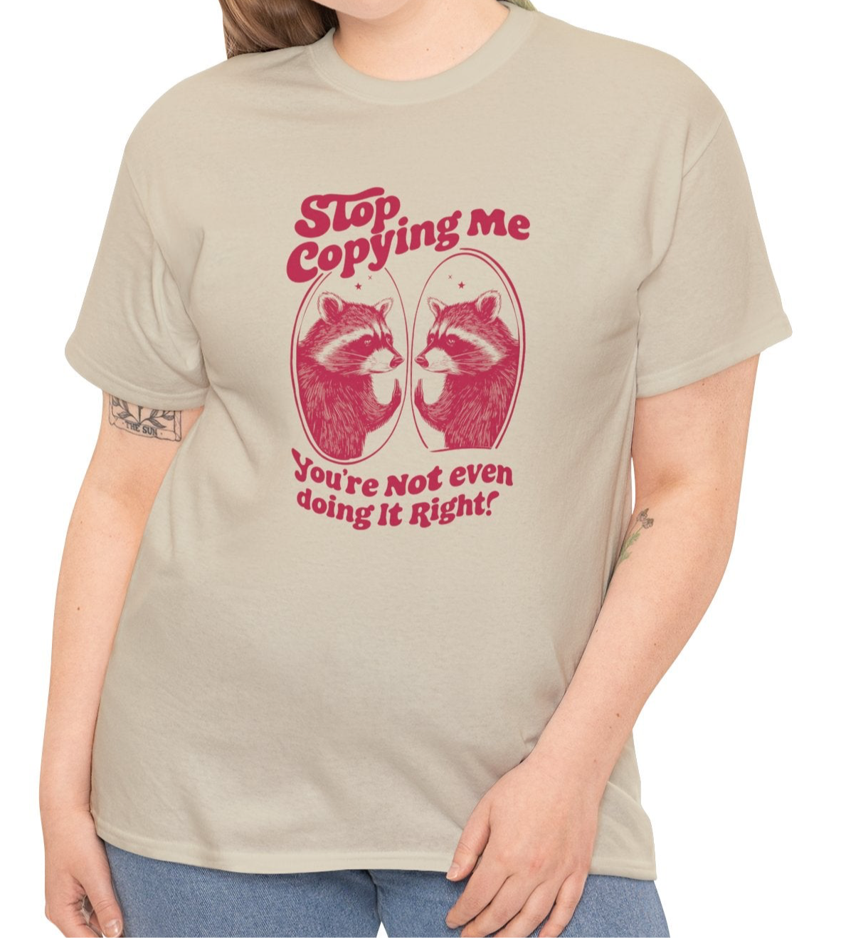 Model wearing a beige T-shirt with "Stop Copying Me" in bold red text and a mirrored raccoon graphic, featuring the tagline "You're Not Even Doing It Right!" Part of the Vivid Divergence Sensory Friendly Unisex Tees Range.