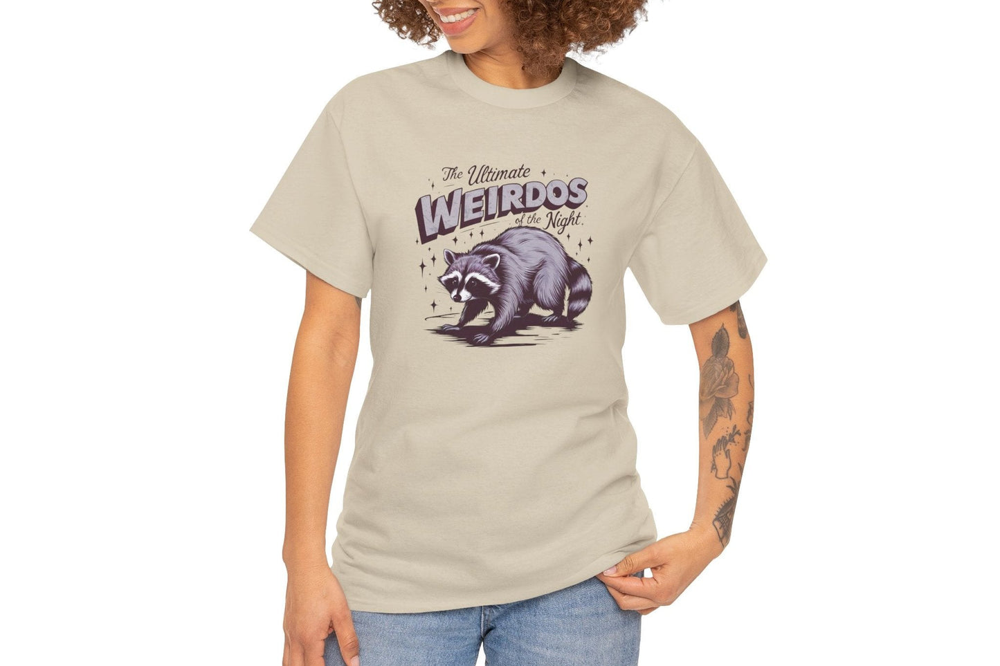 Model wearing a beige T-shirt with "Weirdos of the Night" and an illustrated raccoon graphic in bold purple and black text. Part of the Vivid Divergence Sensory Friendly Unisex Tees Range.