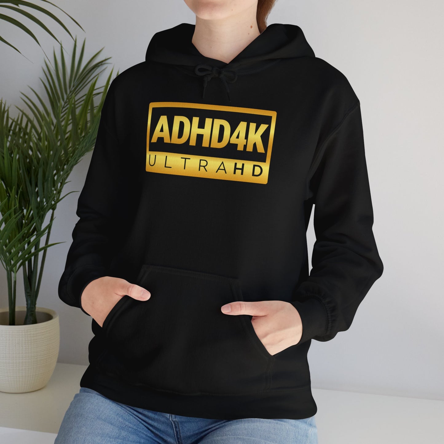Model wearing a black hoodie with the text "ADHD4K UltraHD" in bold yellow and black lettering inside a rectangular design. Part of the Vivid Divergence Sensory Friendly Unisex Hoodie Range.