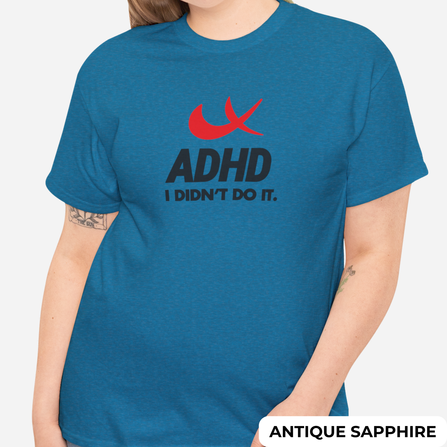 Front view of a blue T-shirt with the phrase "ADHD I Didn't Do It" and a red swoosh parody of the Nike symbol. Part of the Vivid Divergence Sensory Friendly Unisex Tees Range.