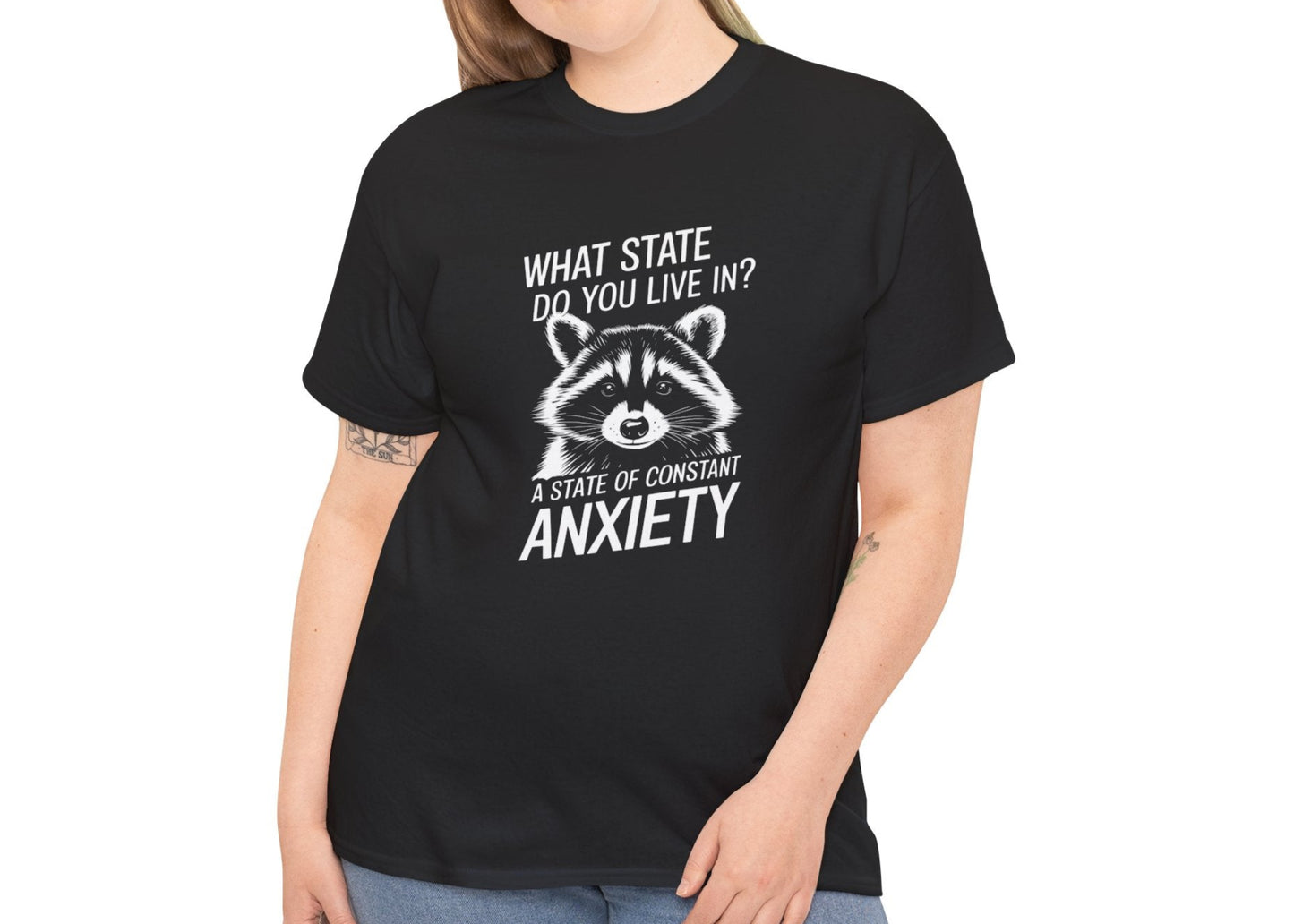 Female model wearing a black T-shirt with a white raccoon graphic and the text "What state do you live in? A constant state of chronic anxiety." Part of the Vivid Divergence Sensory Friendly Unisex Tees Range.