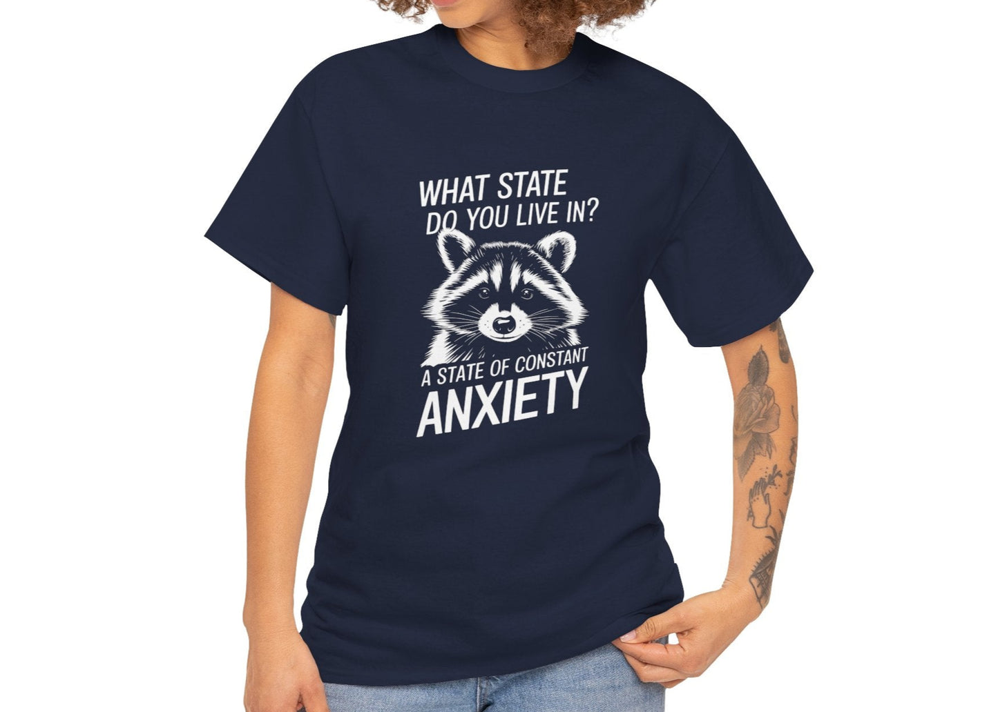Female model wearing a navy blue T-shirt with a white raccoon graphic and the text "What state do you live in? A constant state of chronic anxiety." Part of the Vivid Divergence Sensory Friendly Unisex Tees Range.