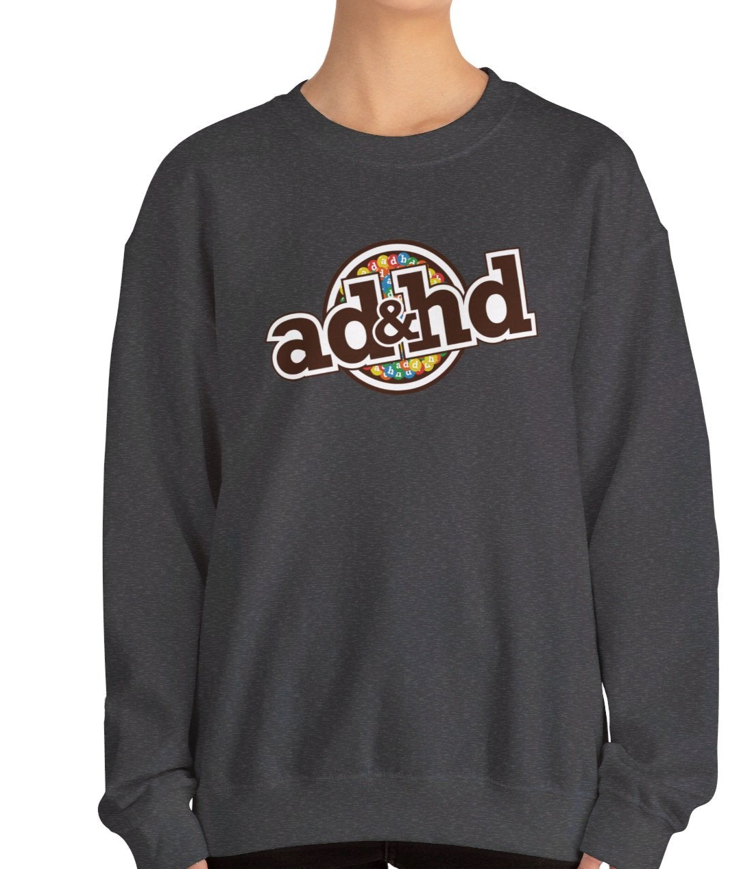 Model wearing a dark gray sweater jumper with an "ADHD" m&m brand parody design in brown and yellow tones. Part of the Vivid Divergence Sensory Friendly Unisex Sweater Jumper Range.