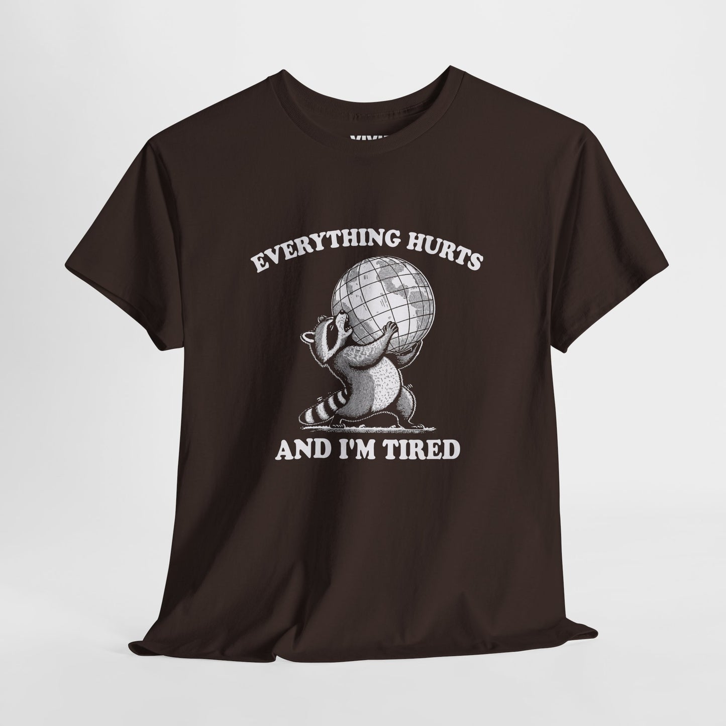 Hanging view of chocolate brown T-shirt featuring a vintage style sketch of a raccoon carrying the world with the phrase “Everything Hurts and I’m Tired.” The official uniform of burnt out. Part of the Vivid Divergence Memewear Collection!