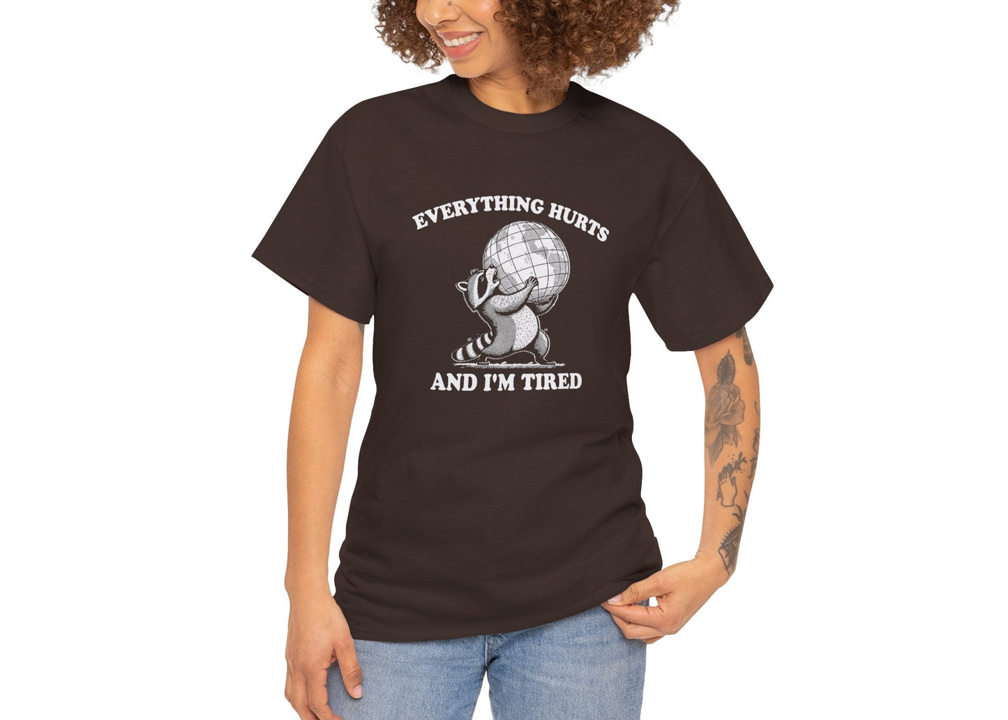 Modeled view of chocolate brown T-shirt featuring a vintage style sketch of a raccoon carrying the world with the phrase “Everything Hurts and I’m Tired.” The official uniform of burnt out. Part of the Vivid Divergence Memewear Collection!