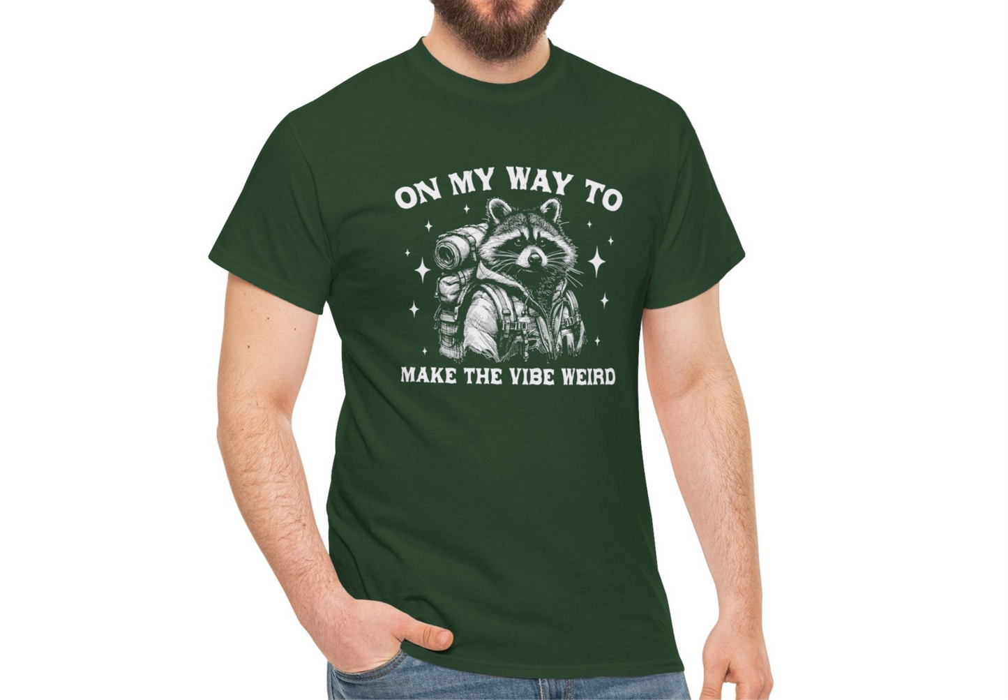 Model in a casual setting wearing a forest green T-shirt with "On My Way to Make the Vibe Weird" and a raccoon graphic in white text. Part of the Vivid Divergence Sensory Friendly Unisex Tees Range.