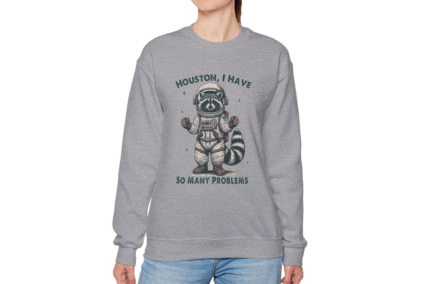 Model wearing a gray sweater jumper with the text "Houston, I Have So Many Problems" and a cartoon raccoon illustration holding a striped object. Part of the Vivid Divergence Sensory Friendly Unisex Sweater Jumper Range.