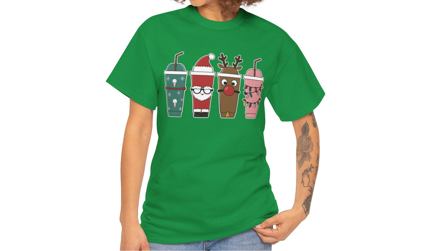 Model wearing a green T-shirt featuring a festive illustration of four iced coffee cups decorated with Christmas designs, styled in a cozy indoor setting. Part of the Vivid Divergence Sensory Friendly Unisex.