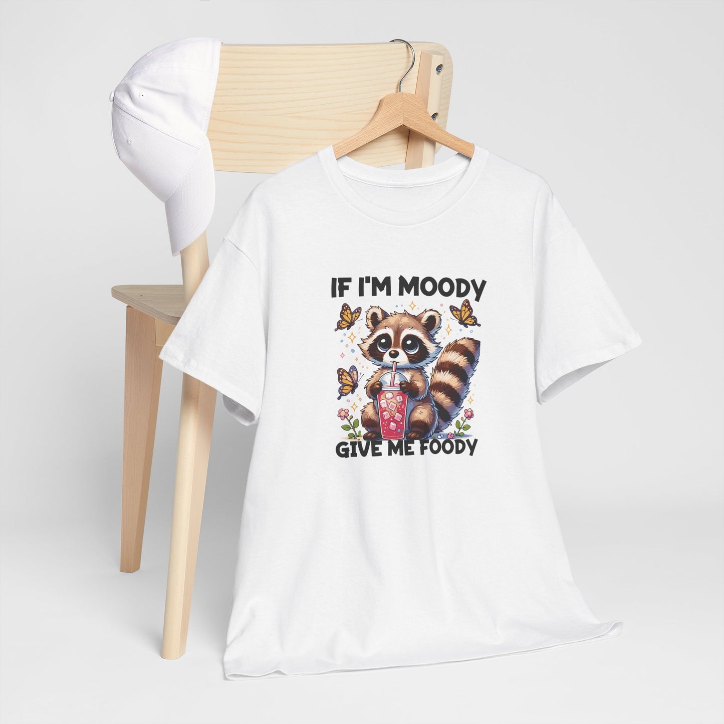 Front hanging view of a white T-shirt featuring a raccoon graphic with food and the text "If I'm Moody, Give Me Foody." Part of the Vivid Divergence Sensory Friendly Unisex Tees Range.