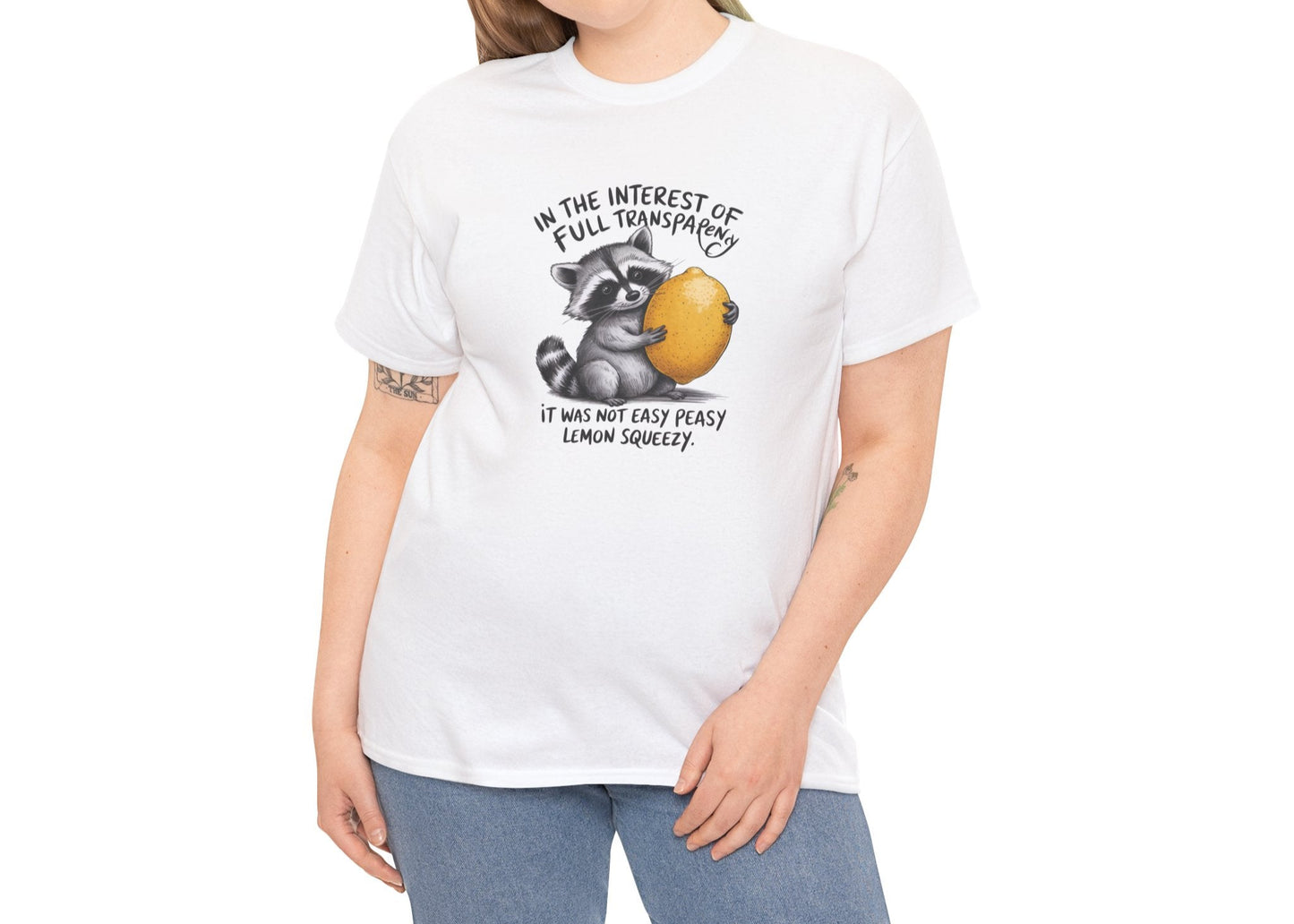 Modeled view of white T-shirt featuring a raccoon holding onto a lemon with the text “In the interest of transparency, it was not easy peasy lemon squeezy.” The emotional squeeze is real. Part of the Vivid Divergence Memewear Collection!
