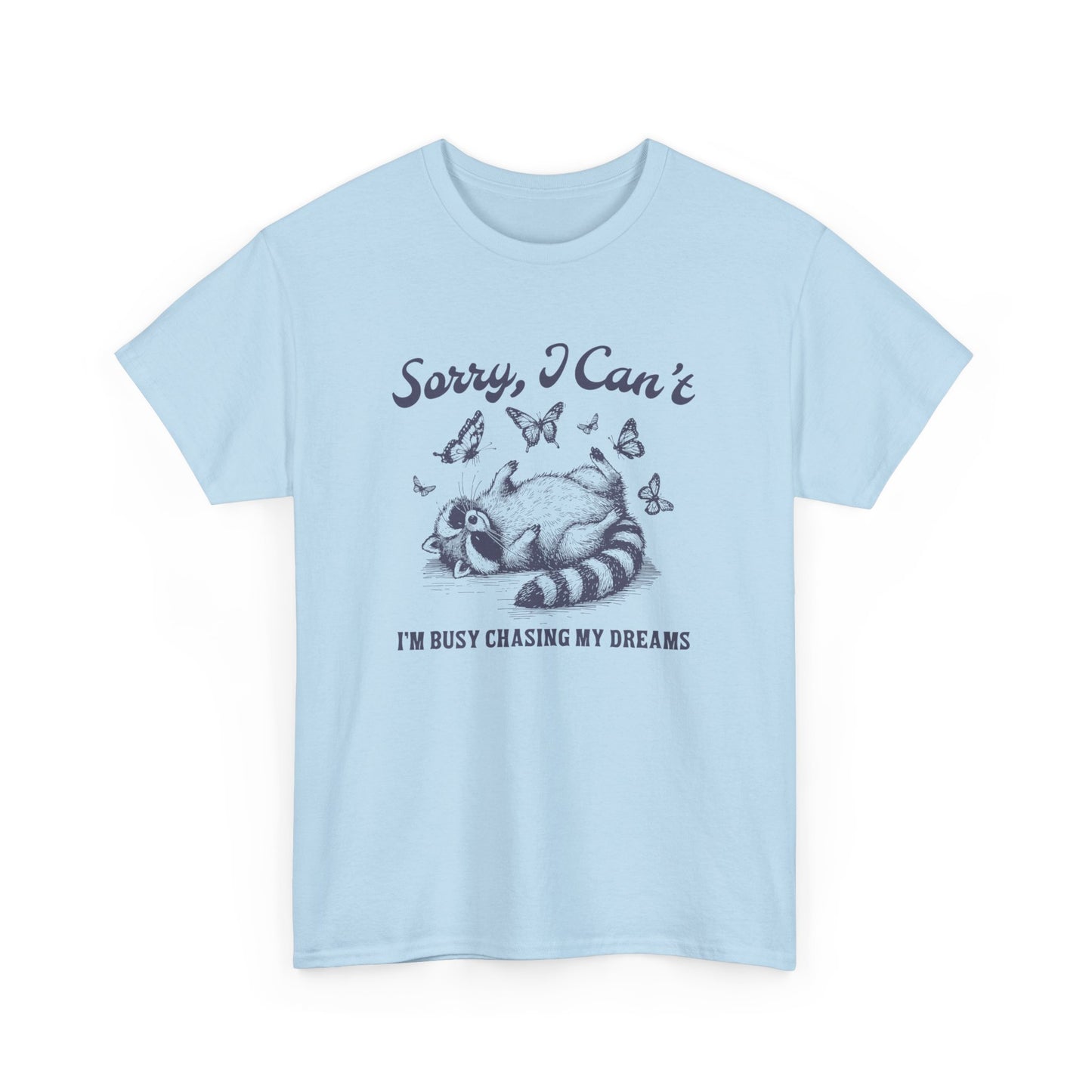 Front view of a light blue T-shirt with "Sorry I Can't, I'm Busy Chasing My Dreams" and a playful sleeping raccoon graphic in black text. Part of the Vivid Divergence Sensory Friendly Unisex Tees Range.