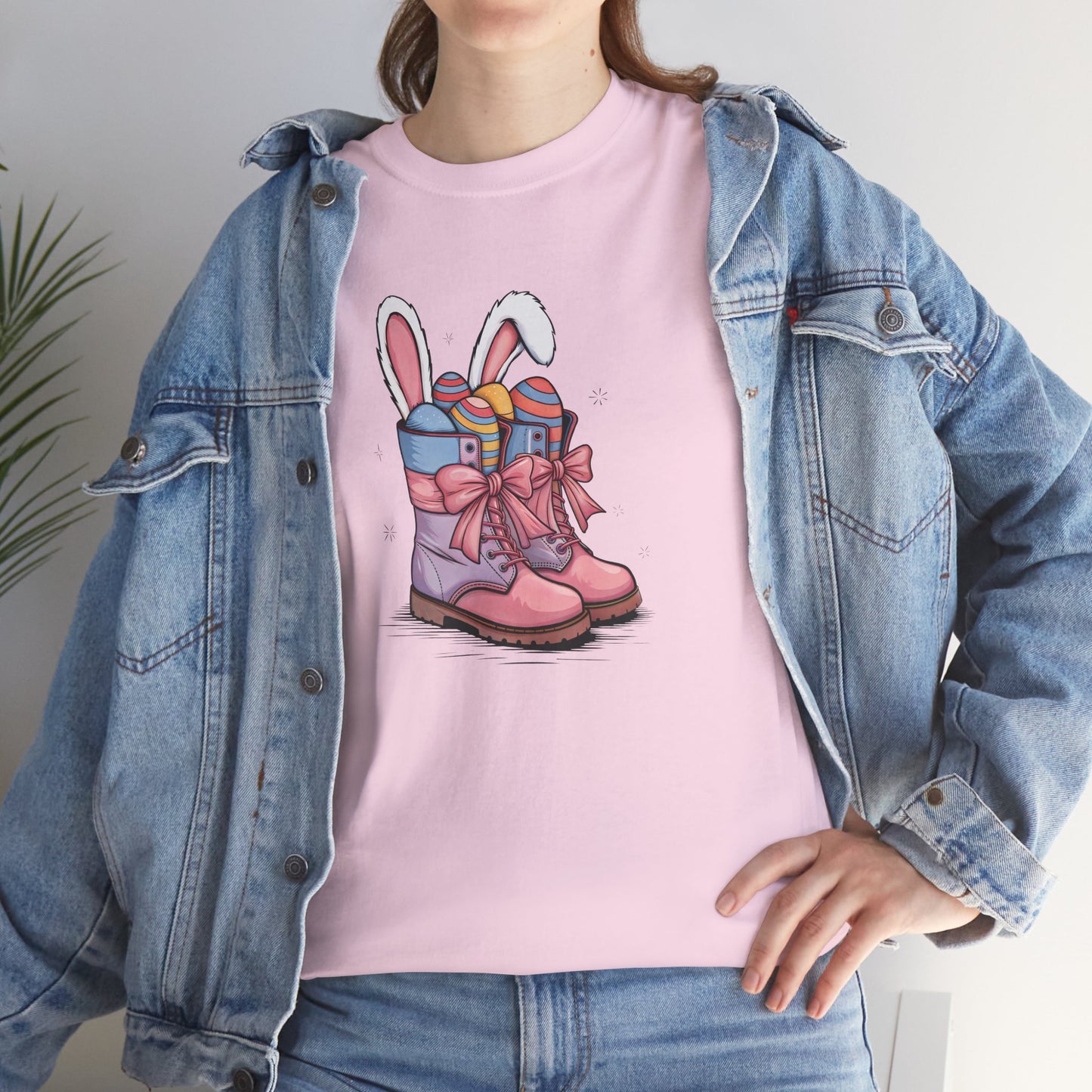 Woman wearing a Light Pink Easter T-shirt with cowgirl boots, bunny ears, and colorful eggs, a soft and stylish spring outfit. Hop into the season in style and shop Easter shirts online today!