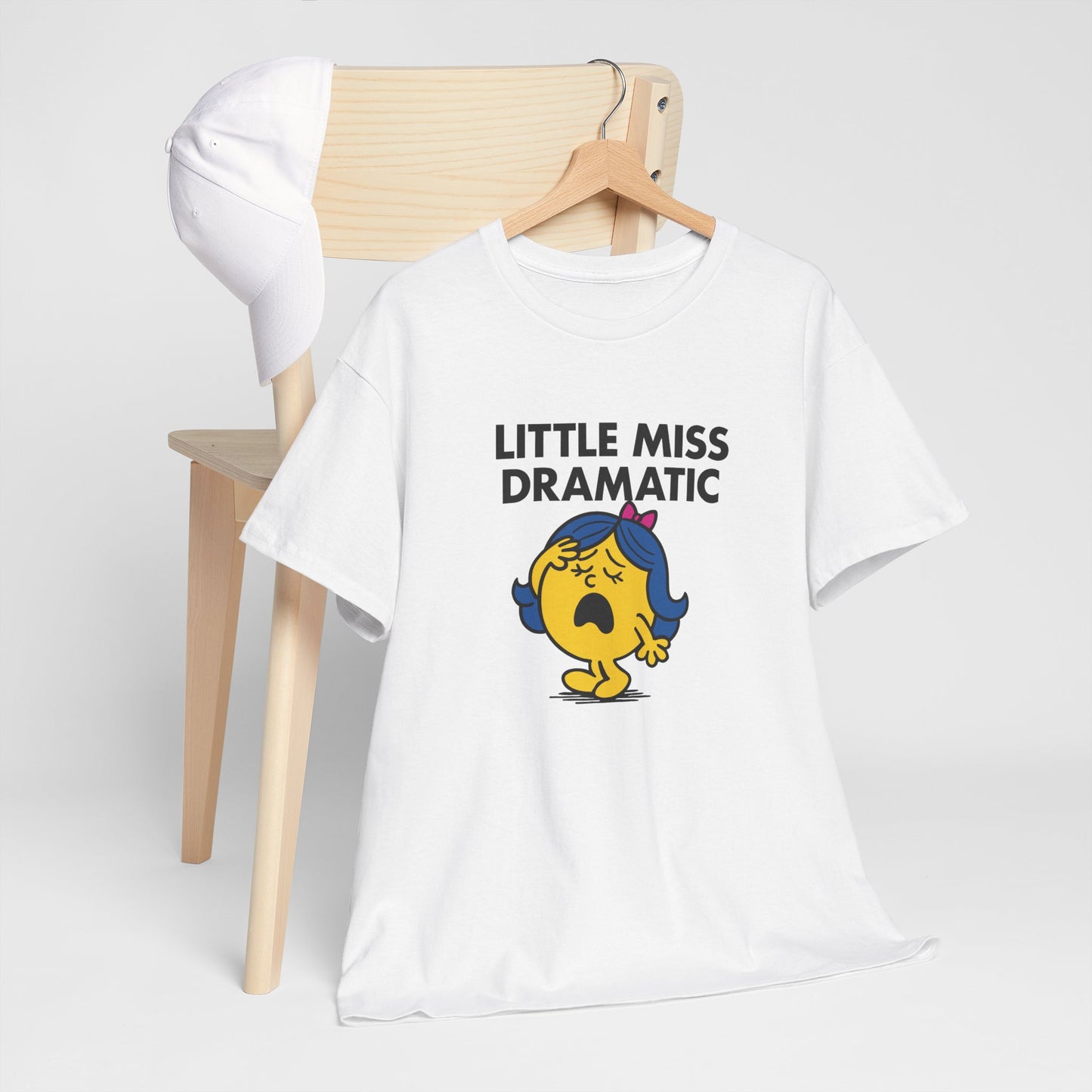 Little Miss Dramatic T-shirt draped over a wooden chair in a clean setup. Part of the Little Miss Meme Character Collection. A Vivid Divergence Sensory Friendly Unisex Tee.