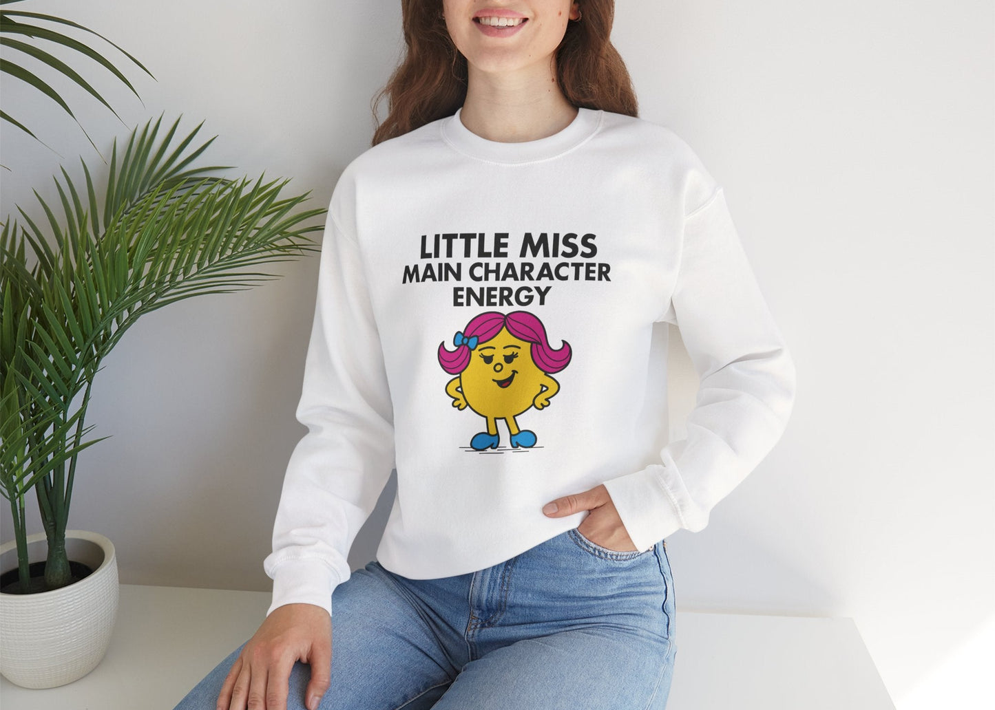 Person wearing the Little Miss Main Character Energy sweatshirt while seated with a smile. Part of the Little Miss Meme Character Collection. A Vivid Divergence Sensory Friendly Sweater Jumper.