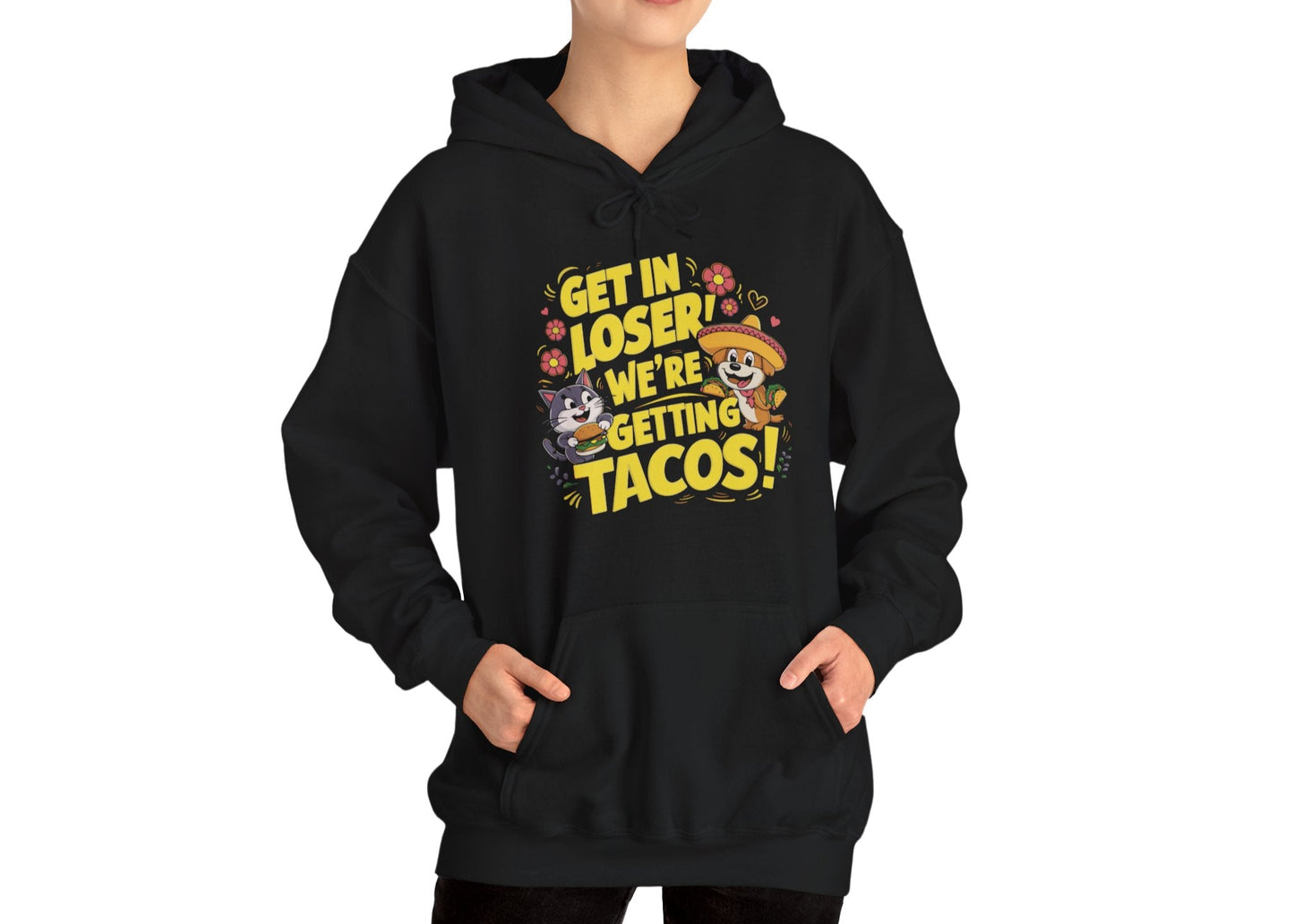Model wearing a black hoodie with colorful cartoon animals and the text "Get in Loser, We're Getting Tacos!" standing with hands in pockets. Part of the Vivid Divergence Sensory Friendly Unisex Hoodie Range.