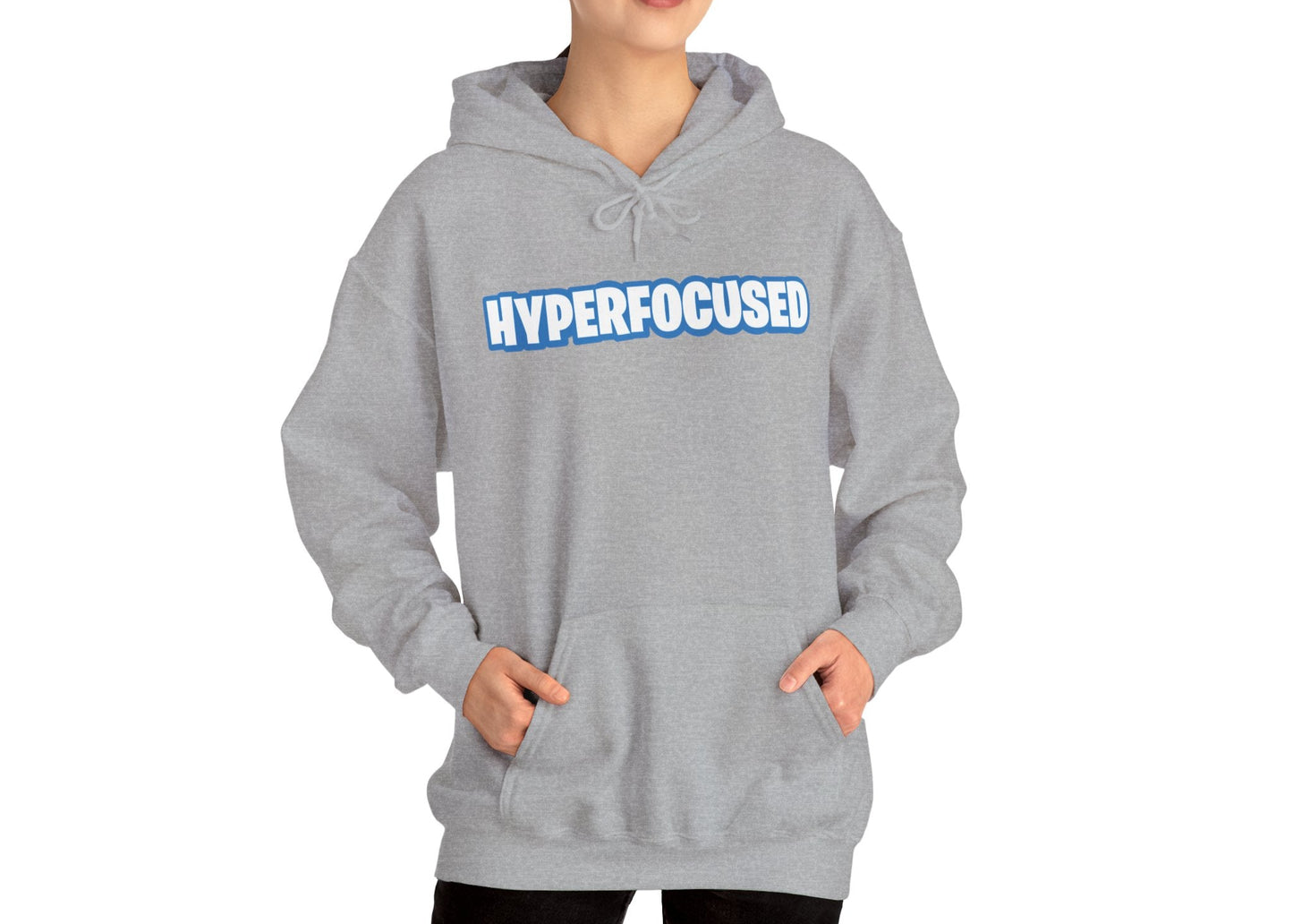Model wearing a gray hoodie with the word "HYPERFOCUSED" in a bold, blue Fortnite-style font, standing with hands in pockets. Part of the Vivid Divergence Sensory Friendly Unisex Hoodie Range.