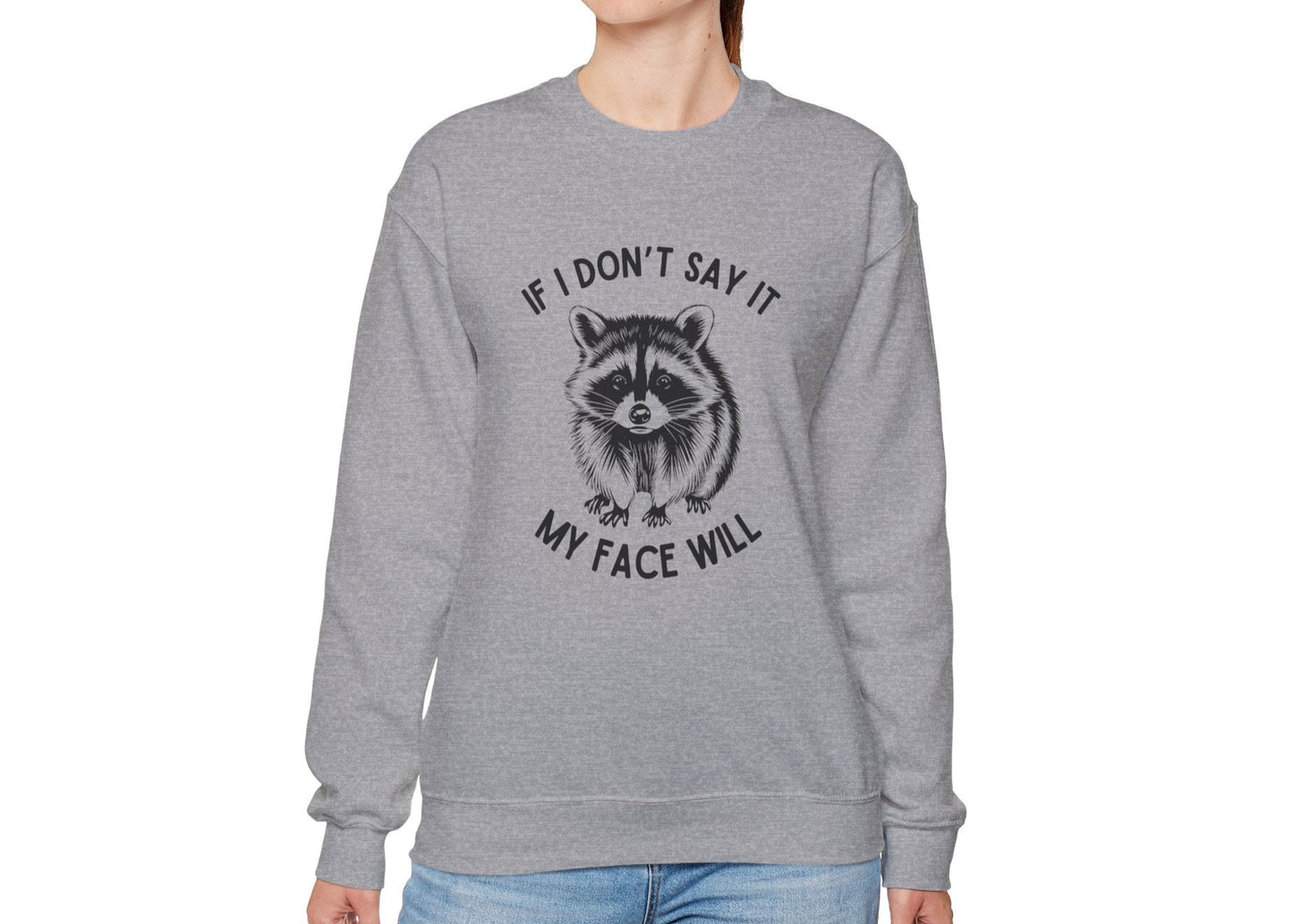 Model wearing a gray sweatshirt with a raccoon graphic and the text "If I Don't Say It, My Face Will," standing with hands at sides. Part of the Vivid Divergence Sensory Friendly Unisex Sweater Jumper Range.