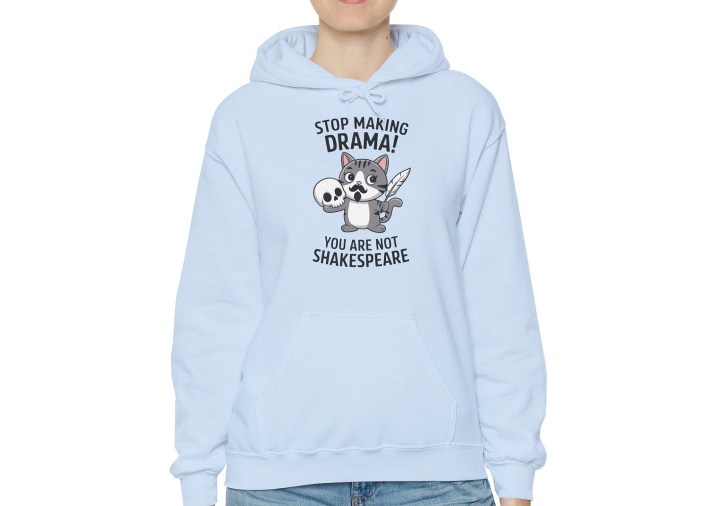 Model wearing a light blue hoodie with a cartoon cat holding a skull and the text "Stop Making Drama! You Are Not Shakespeare," standing with hands at sides. Part of the Vivid Divergence Sensory Friendly Unisex Hoodie Range.