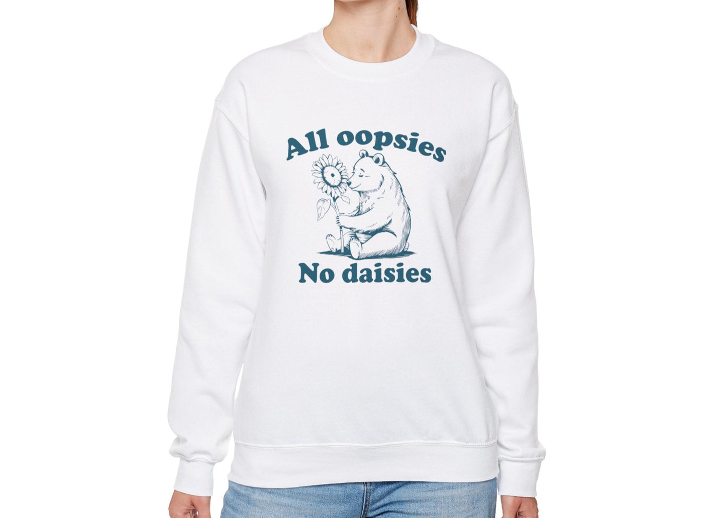 Model wearing a white sweatshirt with a cartoon bear holding a sunflower and the text "All Oopsies, No Daisies," standing with hands at sides. Part of the Vivid Divergence Sensory Friendly Unisex Sweater Jumper Range.