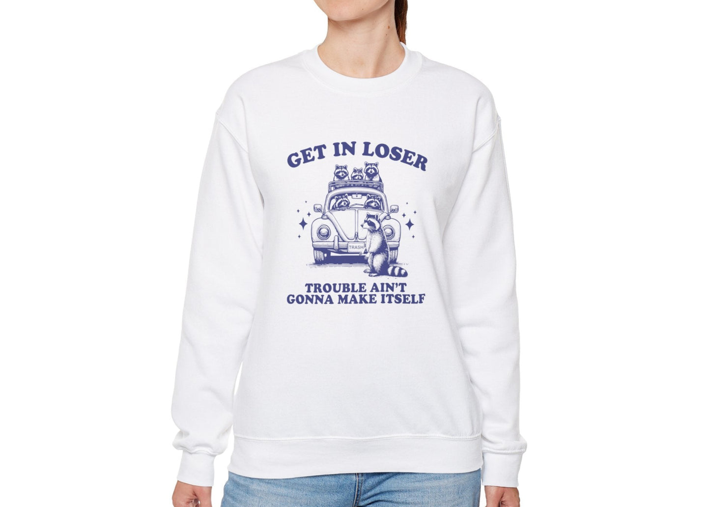 Model wearing a white sweatshirt with "Get in Loser, Trouble Ain't Gonna Cause Itself" in blue letters and a group of raccoons in a car, standing with hands at sides. Part of the Vivid Divergence Sensory Friendly Unisex Sweater Jumper Range.