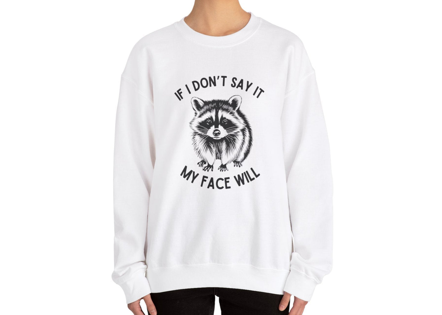 Model wearing a white sweatshirt with a raccoon graphic and the text "If I Don't Say It, My Face Will," standing with hands at sides. Part of the Vivid Divergence Sensory Friendly Unisex Sweater Jumper Range.