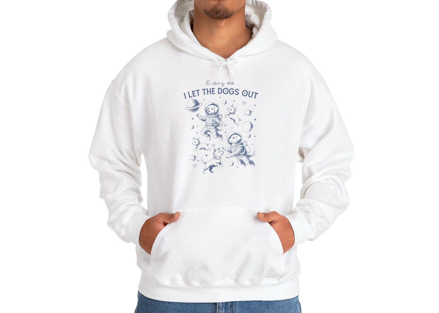 Model wearing a white hoodie with playful dog illustrations and the text "It Was Me, I Let The Dogs Out," standing with hands in pockets. Part of the Vivid Divergence Sensory Friendly Unisex Hoodie Range.