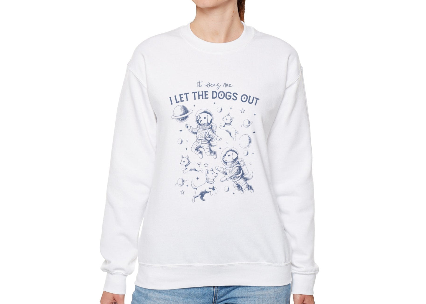 Model wearing a white sweatshirt with playful dog illustrations and the text "It Was Me, I Let The Dogs Out," standing with hands at sides. Part of the Vivid Divergence Sensory Friendly Unisex Sweater Jumper Range.