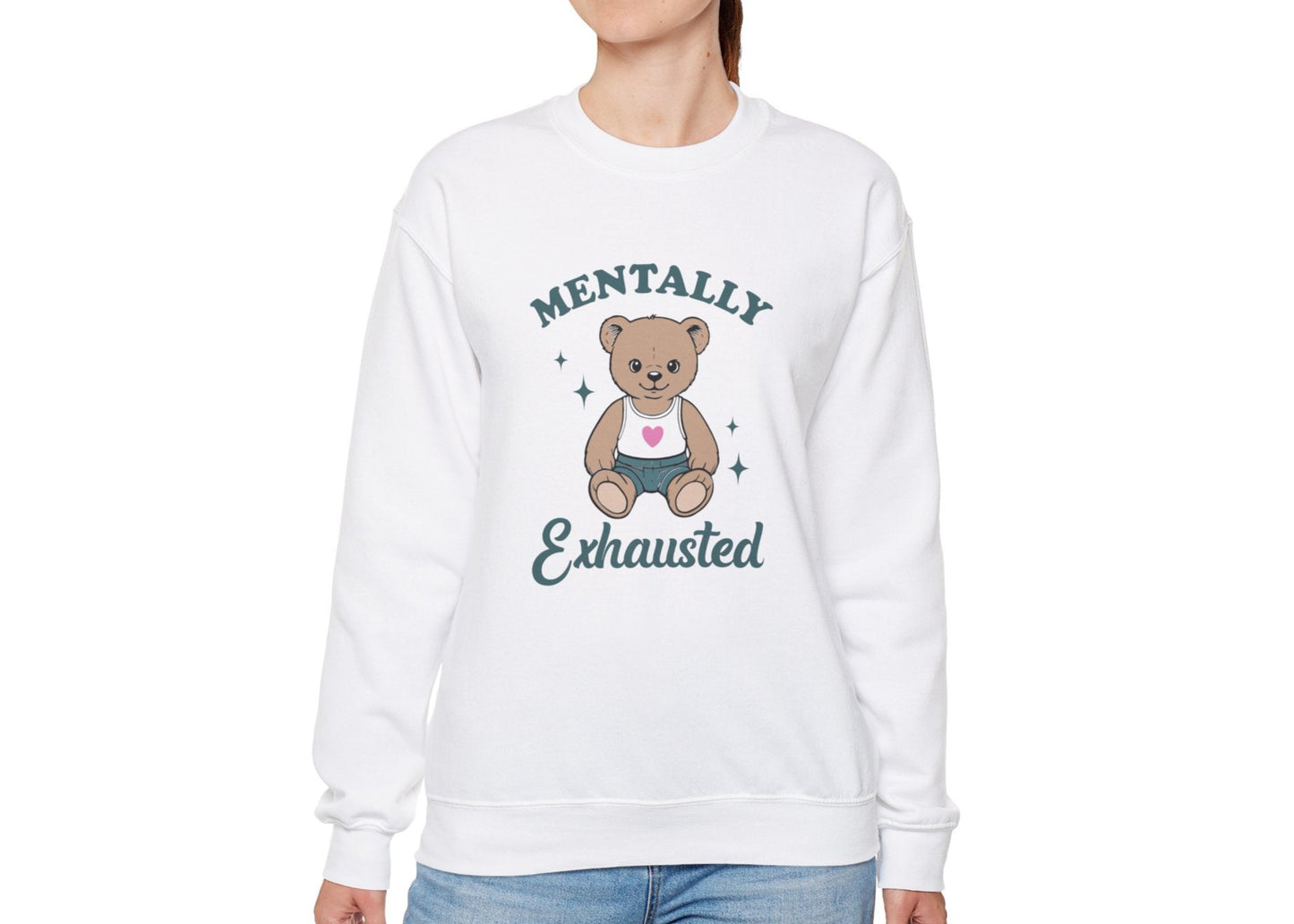 Model wearing a white sweatshirt with a cute teddy bear wearing an apron and the text "Mentally Exhausted," standing with hands at sides. Part of the Vivid Divergence Sensory Friendly Unisex Sweater Jumper Range.