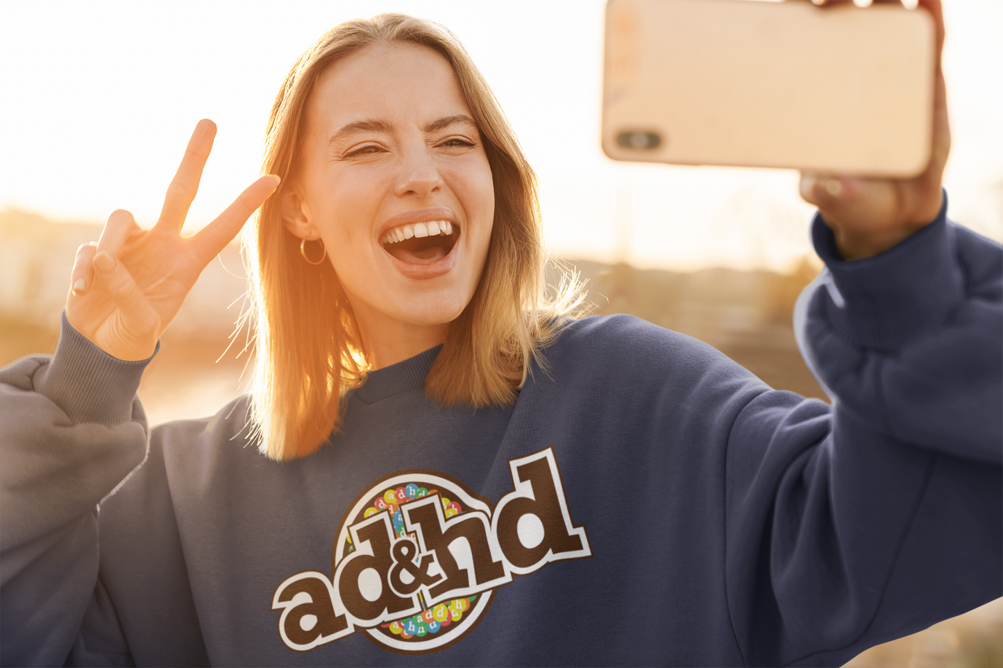 Model wearing a navy blue sweater jumper with an "ADHD" m&m brand parody design in brown and yellow tones. Part of the Vivid Divergence Sensory Friendly Unisex Sweater Jumper Range.