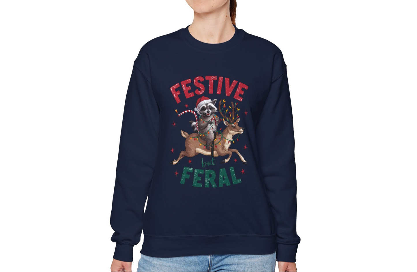 Model wearing a navy blue sweatshirt featuring a festive raccoon holding Christmas lights and the text "Festive but Feral," styled in a casual holiday setting. Part of the Vivid Divergence Sensory Friendly Unisex Sweater Jumper Range.