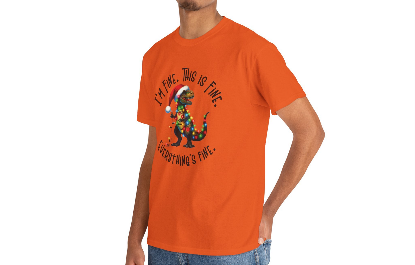 Model wearing an orange T-shirt featuring a festive illustration of a dinosaur tangled in Christmas lights with the text "I’m Fine. This is Fine. Everything is Fine," styled casually. Part of the Vivid Divergence Sensory Friendly Unisex Tees Range.