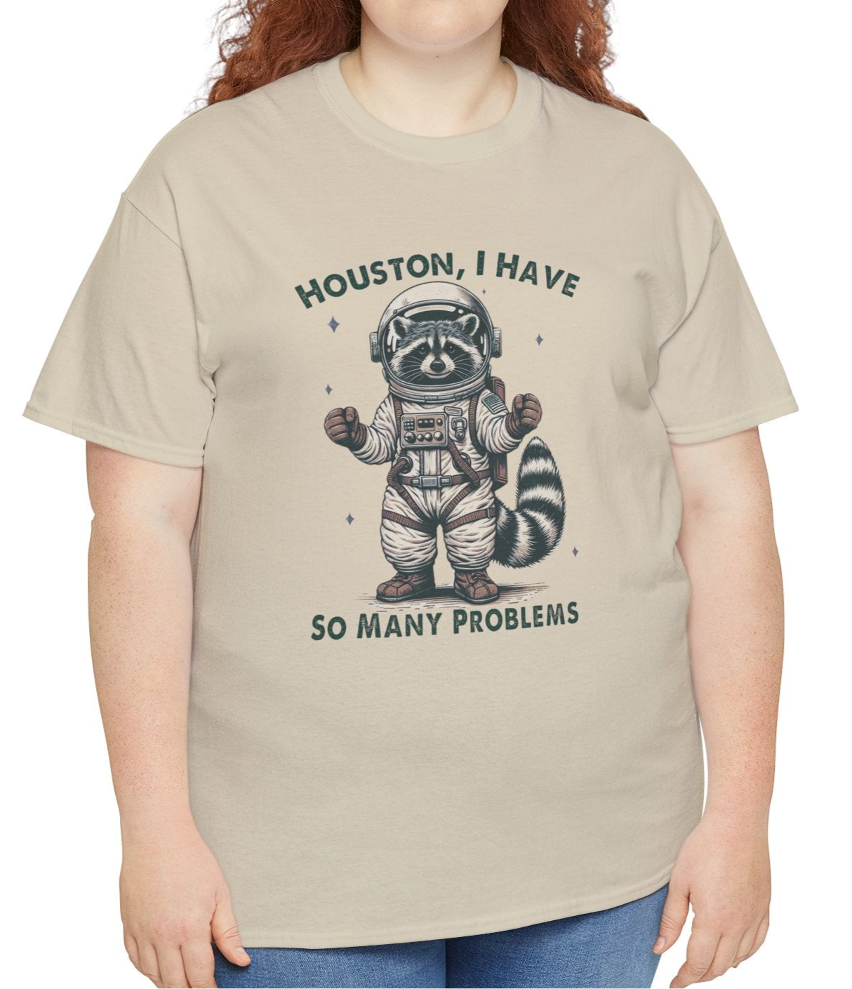A person wearing a beige T-shirt with an astronaut raccoon graphic and the text "Houston, I Have So Many Problems." Part of the Vivid Divergence Sensory Friendly Unisex Tees Range.