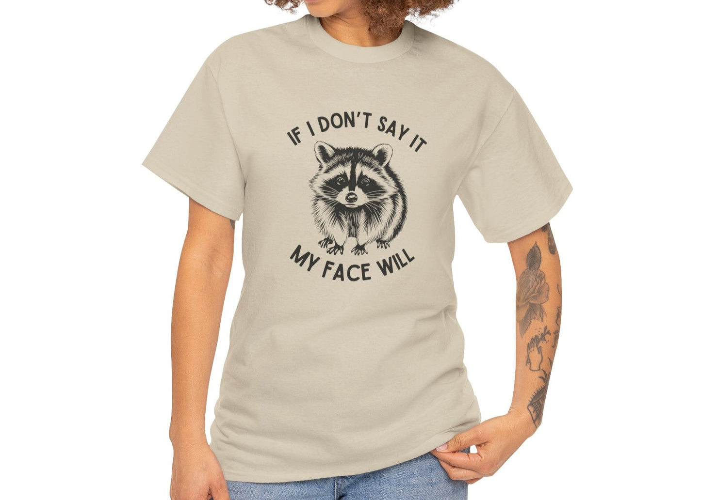 A person wearing a beige T-shirt with a raccoon face graphic and the text "If I Don't Say It, My Face Will." Part of the Vivid Divergence Sensory Friendly Unisex Tees Range.