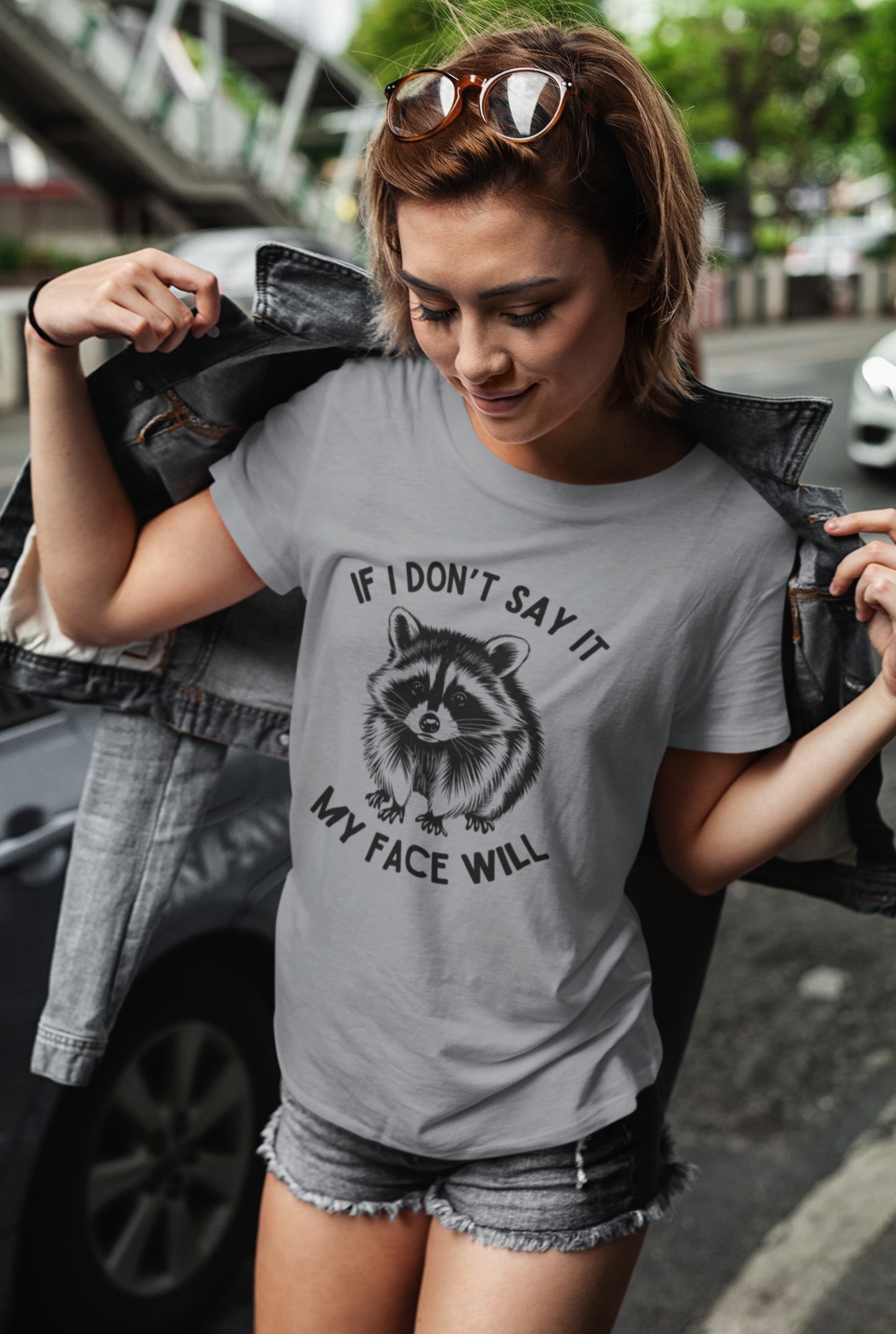 A person wearing a gray T-shirt with a raccoon face graphic and the text "If I Don't Say It, My Face Will." Part of the Vivid Divergence Sensory Friendly Unisex Tees Range.