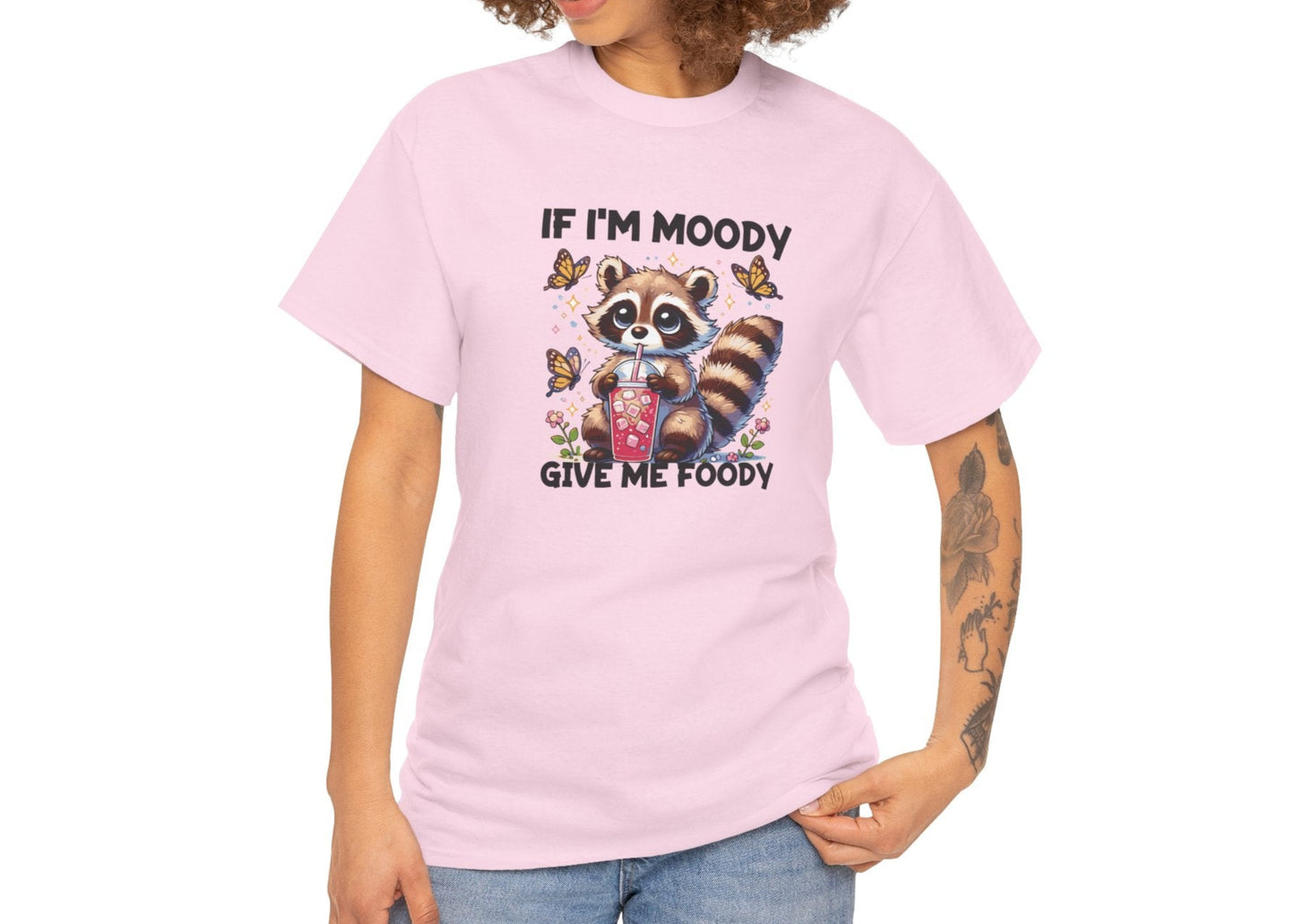 A person wearing a pink T-shirt with a raccoon graphic and the text "If I'm Moody, Give Me Foody." Part of the Vivid Divergence Sensory Friendly Unisex Tees Range.