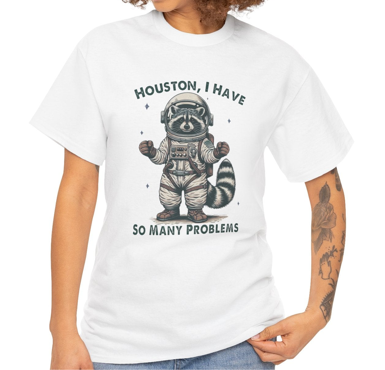A person wearing a white T-shirt with an astronaut raccoon graphic and the text "Houston, I Have So Many Problems." Part of the Vivid Divergence Sensory Friendly Unisex Tees Range.