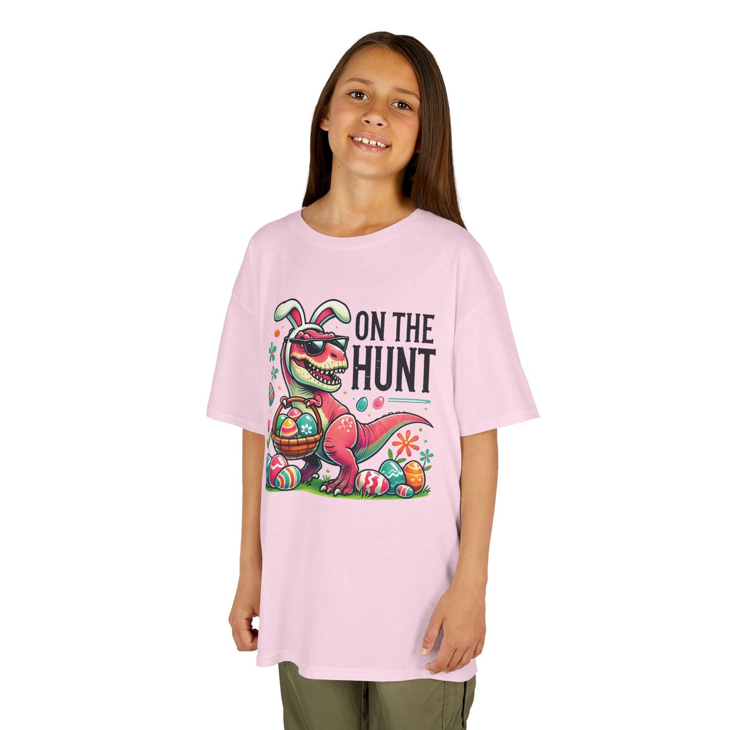 Child wearing a pink Easter T-shirt with a dinosaur, "On the Hunt" text, and vibrant eggs. A stylish and playful Easter outfit. Hop into the season in style and shop Easter shirts online today!