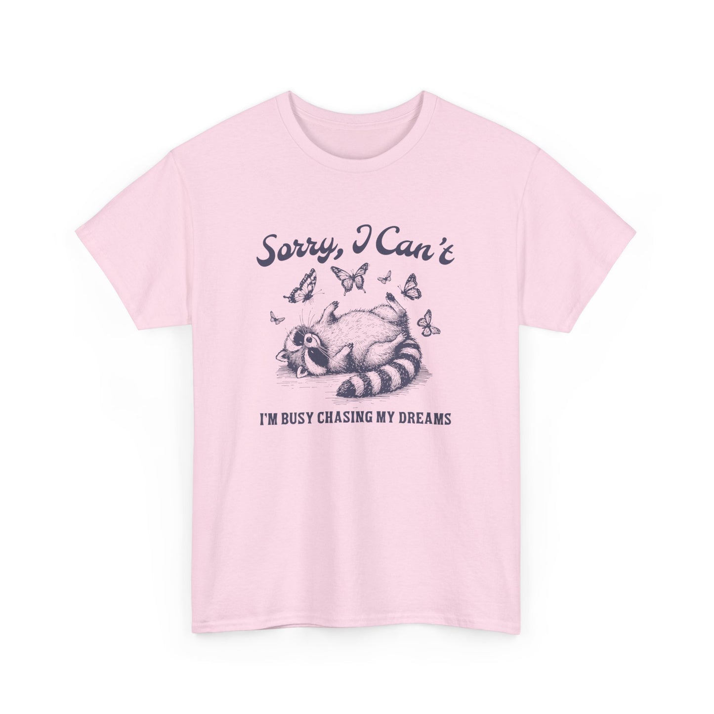 Front view of a pink T-shirt with "Sorry I Can't, I'm Busy Chasing My Dreams" and a playful sleeping raccoon graphic in black text. Part of the Vivid Divergence Sensory Friendly Unisex Tees Range.