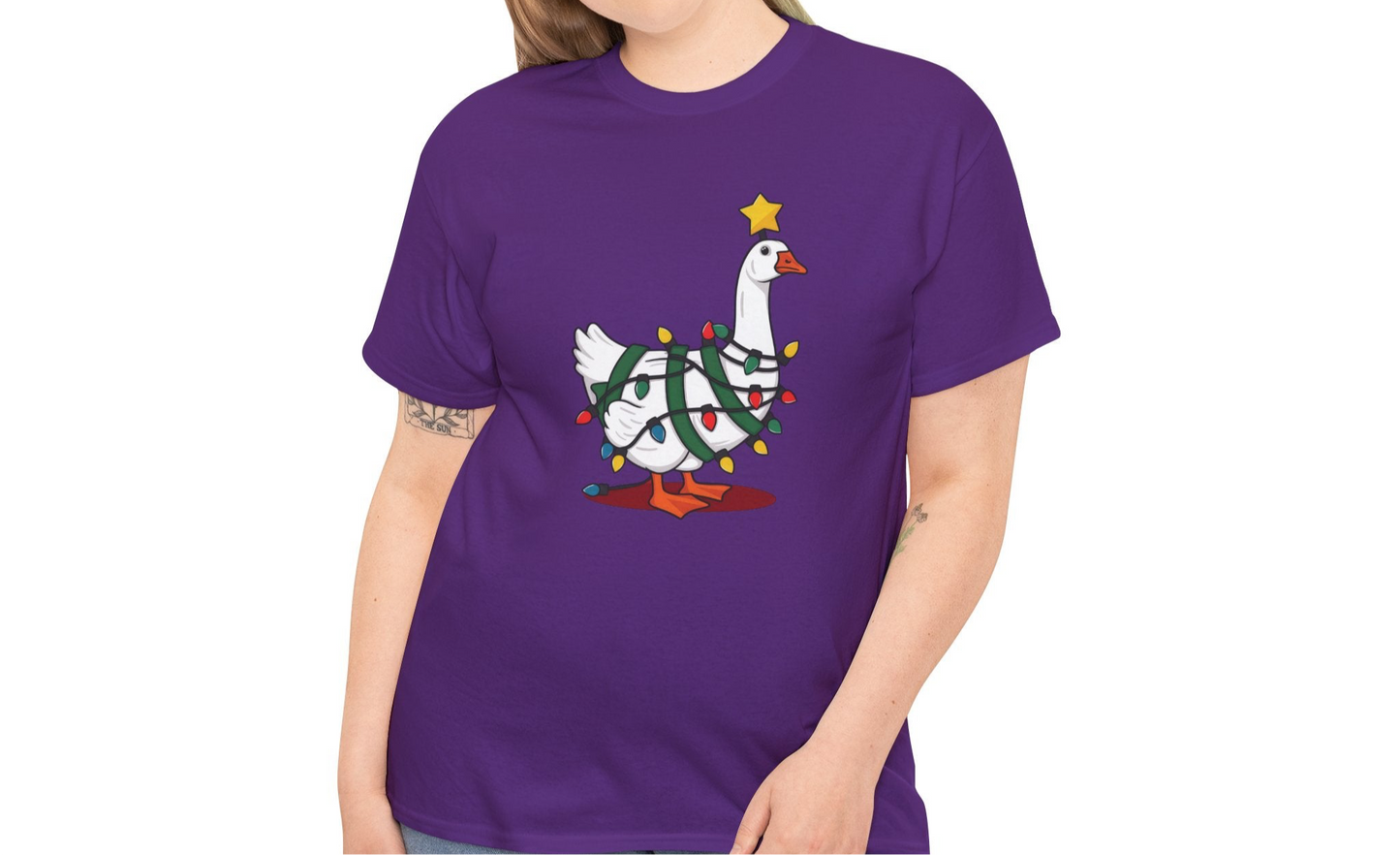 Model wearing a purple T-shirt featuring a festive illustration of a goose wearing a Santa hat and stringing Christmas lights, with the text "Goose on the Loose." Part of the Vivid Divergence Sensory Friendly Unisex Tees Range.