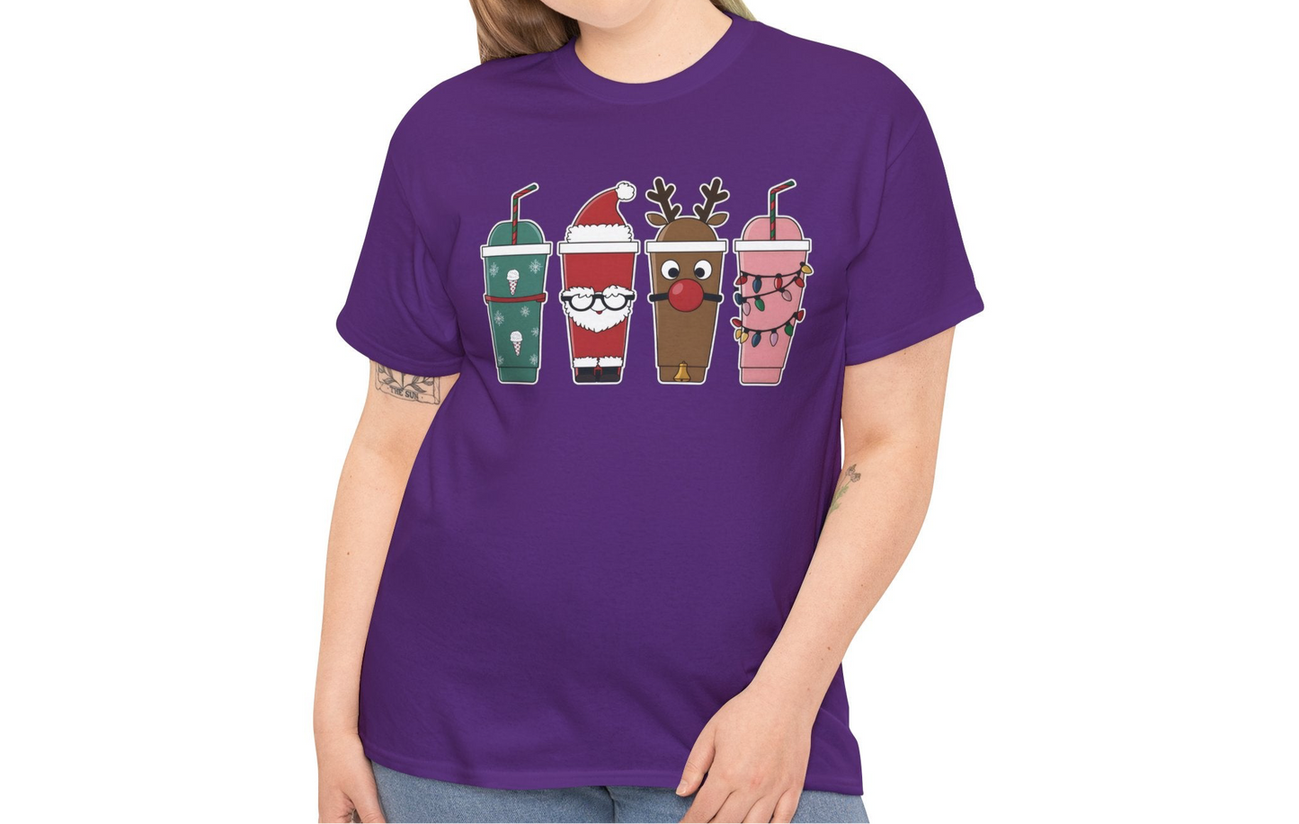 Model wearing a purple T-shirt featuring a festive illustration of four iced coffee cups decorated with Christmas designs, styled in a cozy indoor setting. Part of the Vivid Divergence Sensory Friendly Unisex Tees Range.