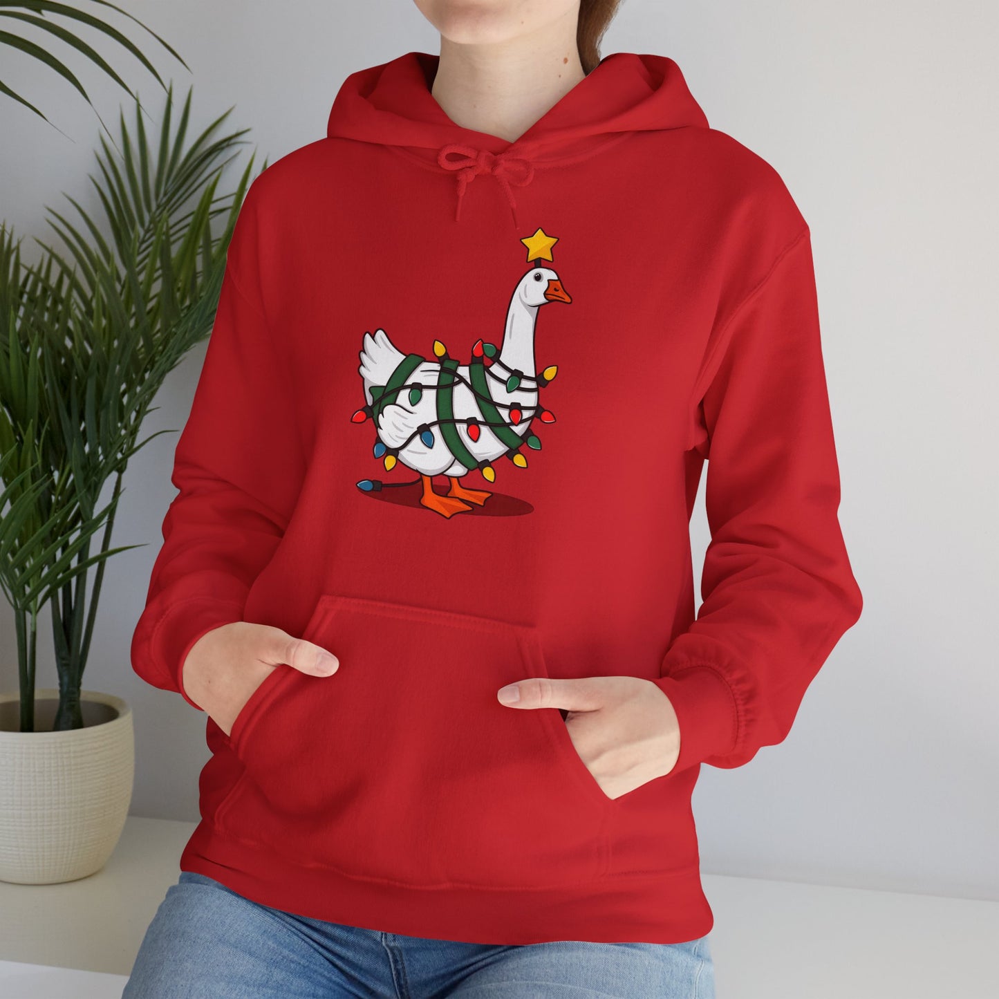 Model wearing a red hoodie featuring a festive illustration of a goose wearing a Santa hat and stringing Christmas lights, with the text "Goose on the Loose." Part of the Vivid Divergence Sensory Friendly Unisex Hoodie Range.
