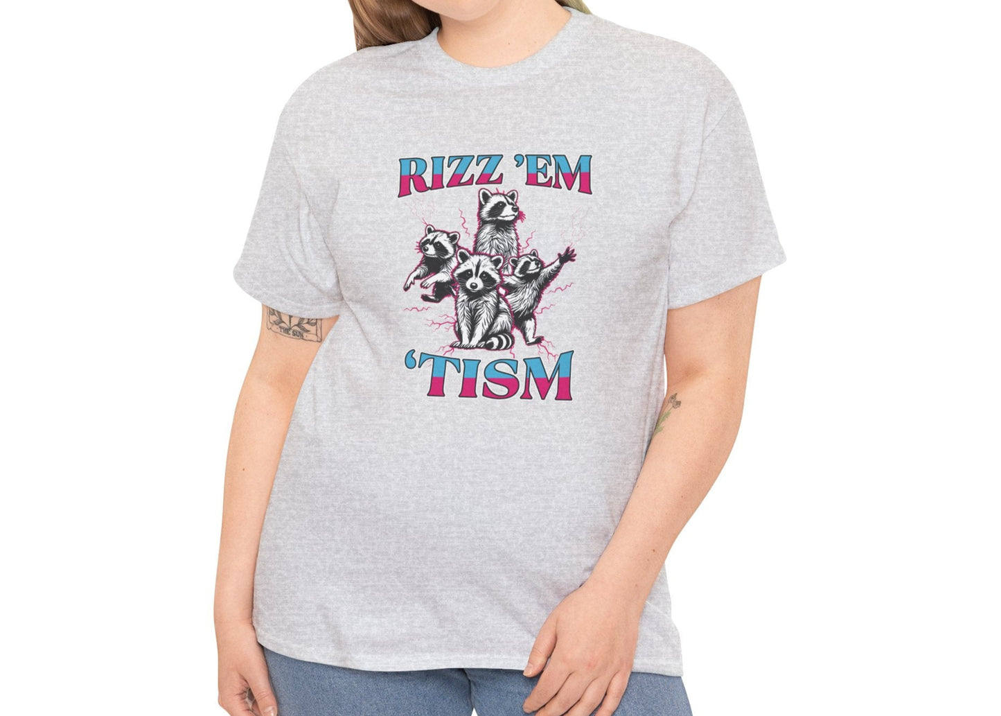 Woman wearing a light gray "RIZZ 'EM 'TISM" T-shirt with raccoon illustration, smiling and posing. Part of the Vivid Divergence Sensory Friendly Unisex Tees Range.