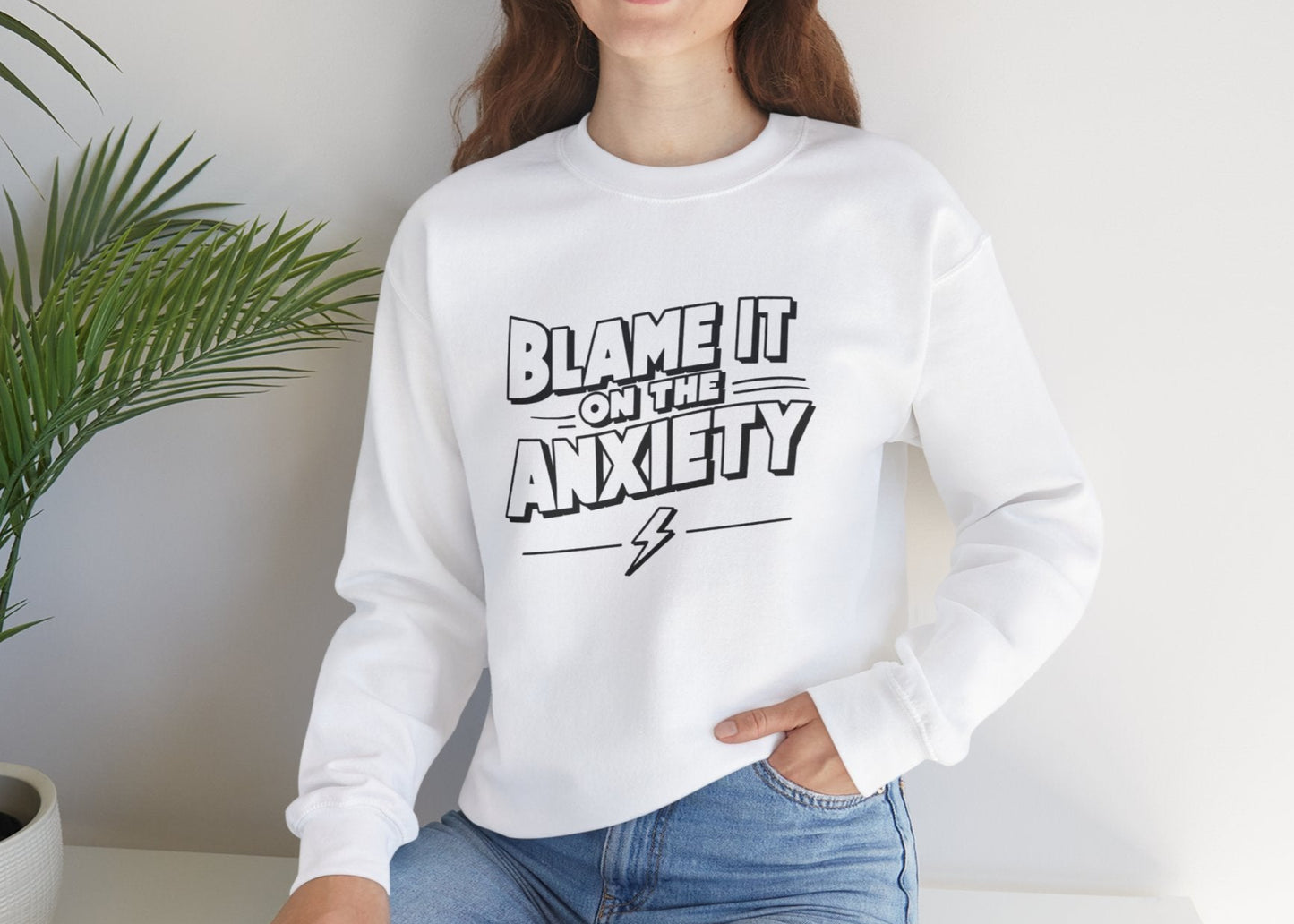 Model seated, wearing a white sweatshirt with bold text that reads "Blame It on the Anxiety." Part of the Vivid Divergence Sensory Friendly Unisex Sweater Jumper Range.