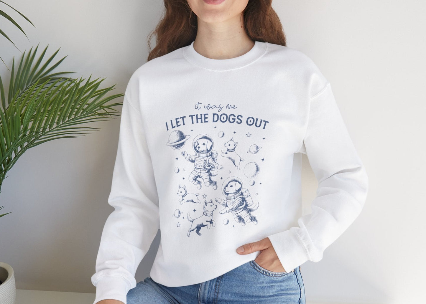 Model seated, wearing a white sweatshirt with playful dog illustrations and the text "It Was Me, I Let The Dogs Out." Part of the Vivid Divergence Sensory Friendly Unisex Sweater Jumper Range.