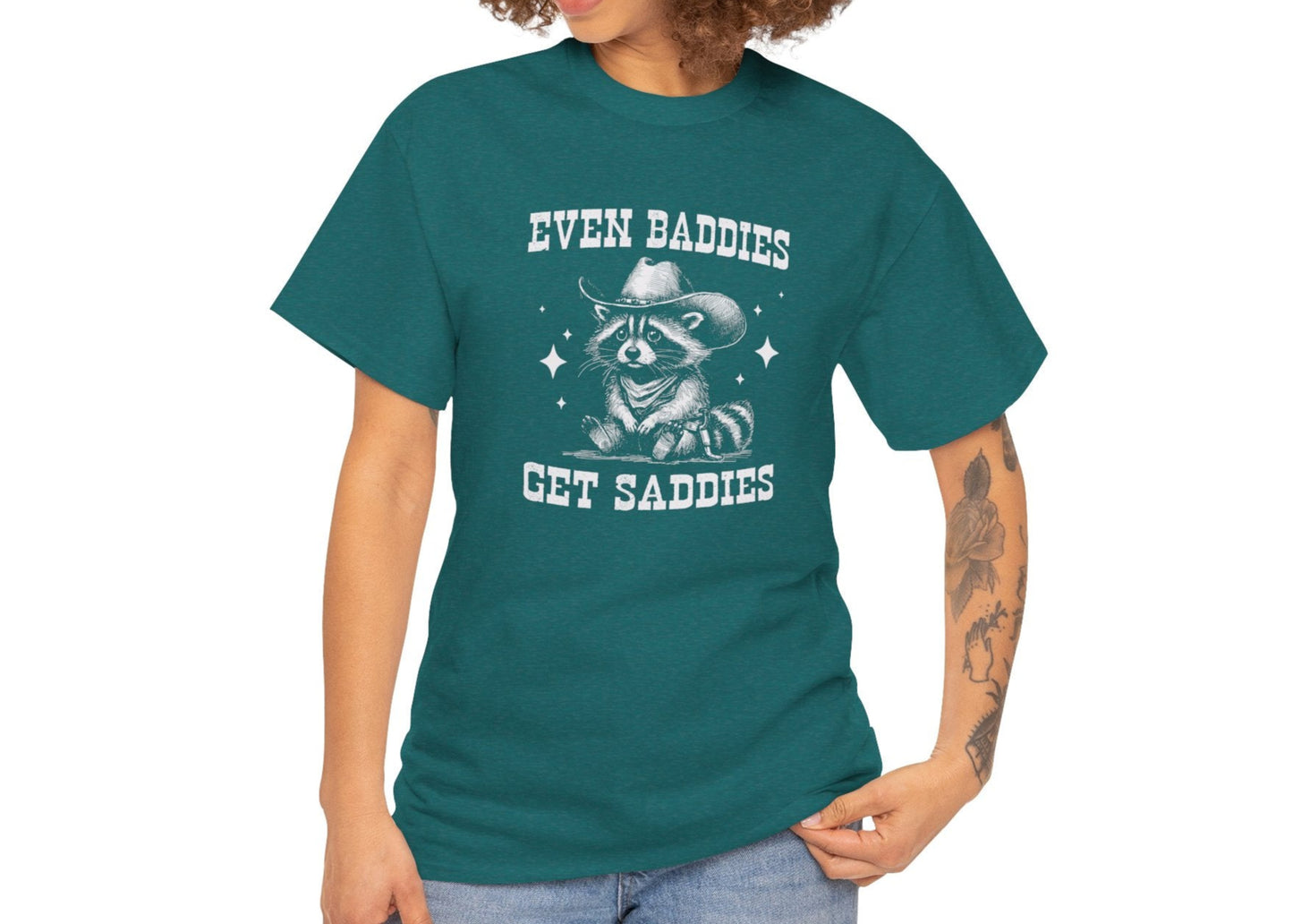 Model wearing a teal T-shirt with the text "Even Baddies Get Saddies" and a crying eye graphic, casual fit. Part of the Vivid Divergence Sensory Friendly Unisex Tees Range.
